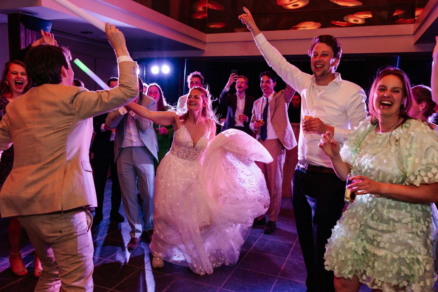 Bride in a white gown celebrates joyfully with groom and guests on the wedding dance floor.