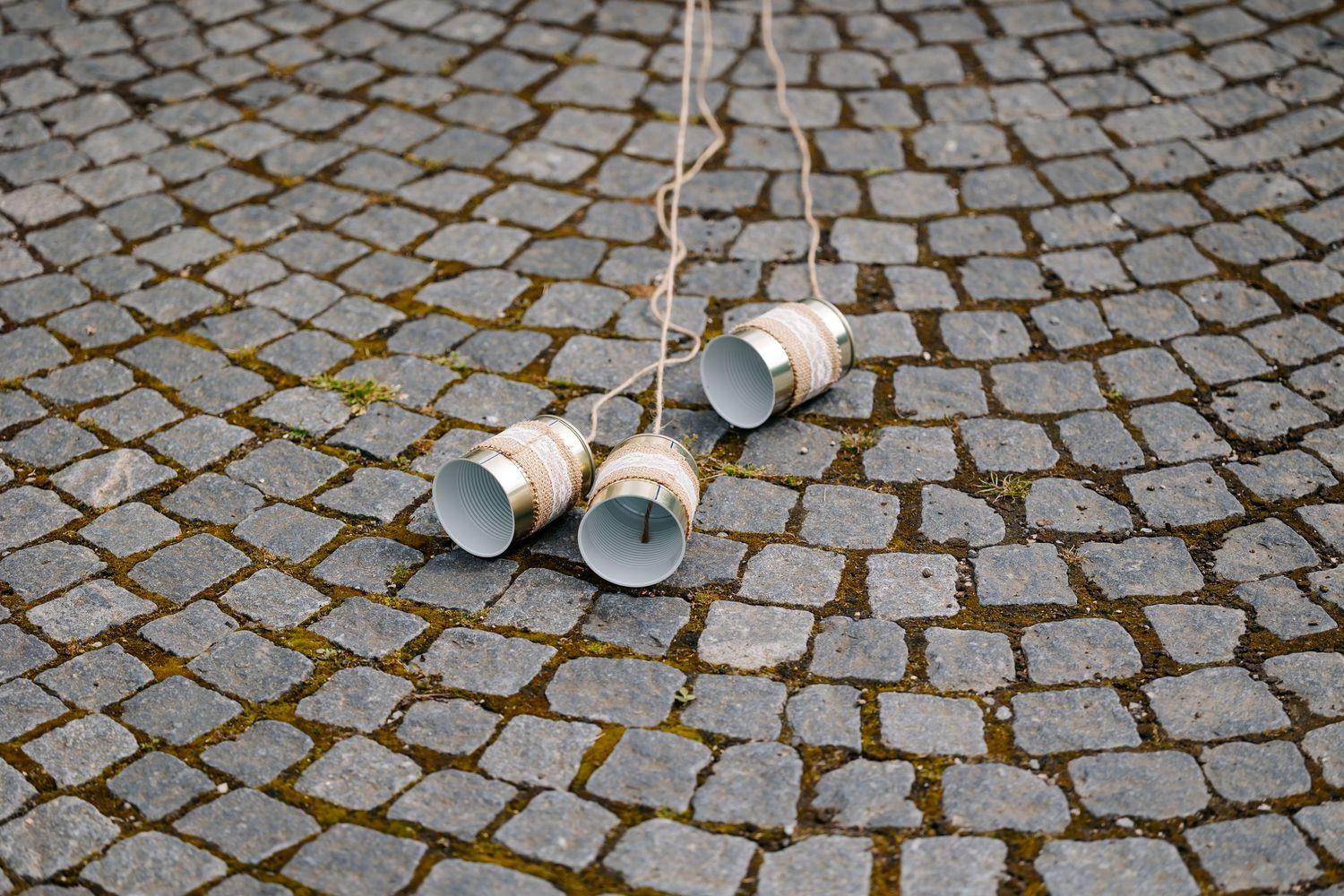 Two tin can telephones connected by string lying on cobblestone pavement.