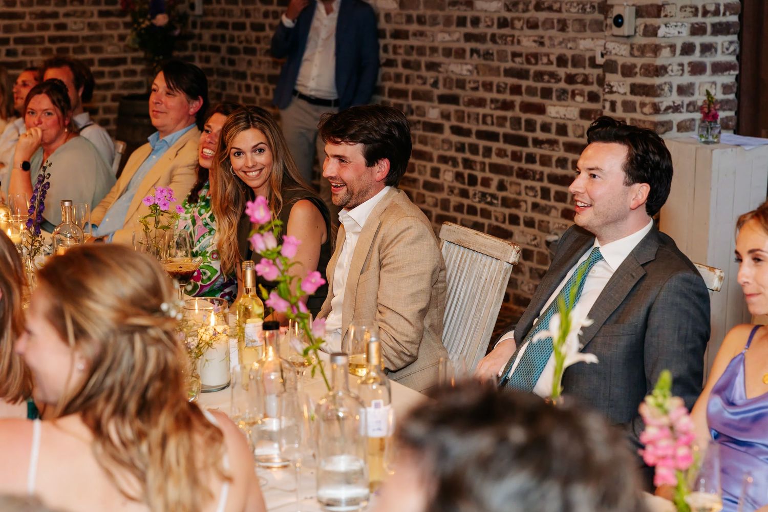 Smiling wedding guests seated at a candlelit reception table adorned with colorful floral arrangements.