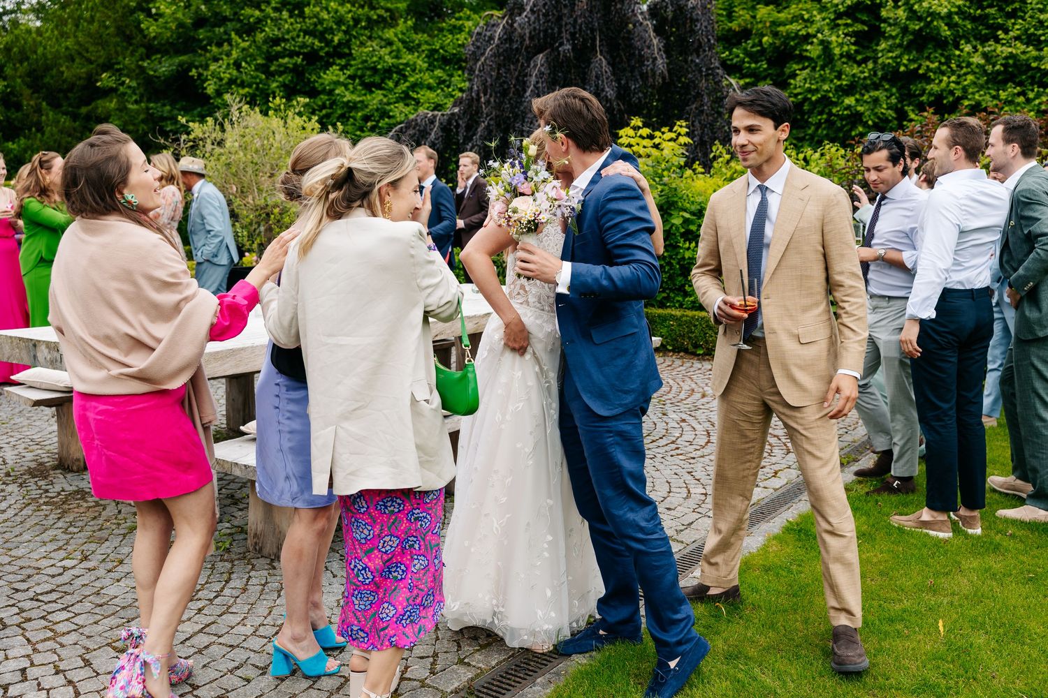 A bride and groom greet guests near a fountain at their outdoor wedding reception.
