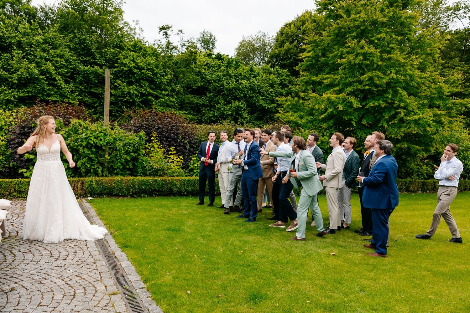 A bride prepares to toss her bouquet to a crowd of eager male guests at an outdoor wedding.
