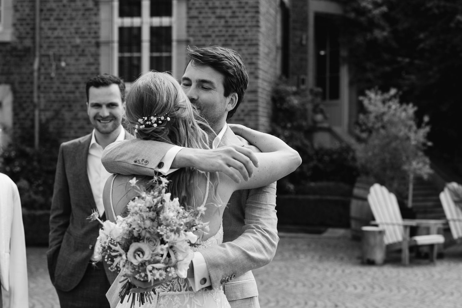 Black and white photo of bride and groom embracing at outdoor wedding celebration.