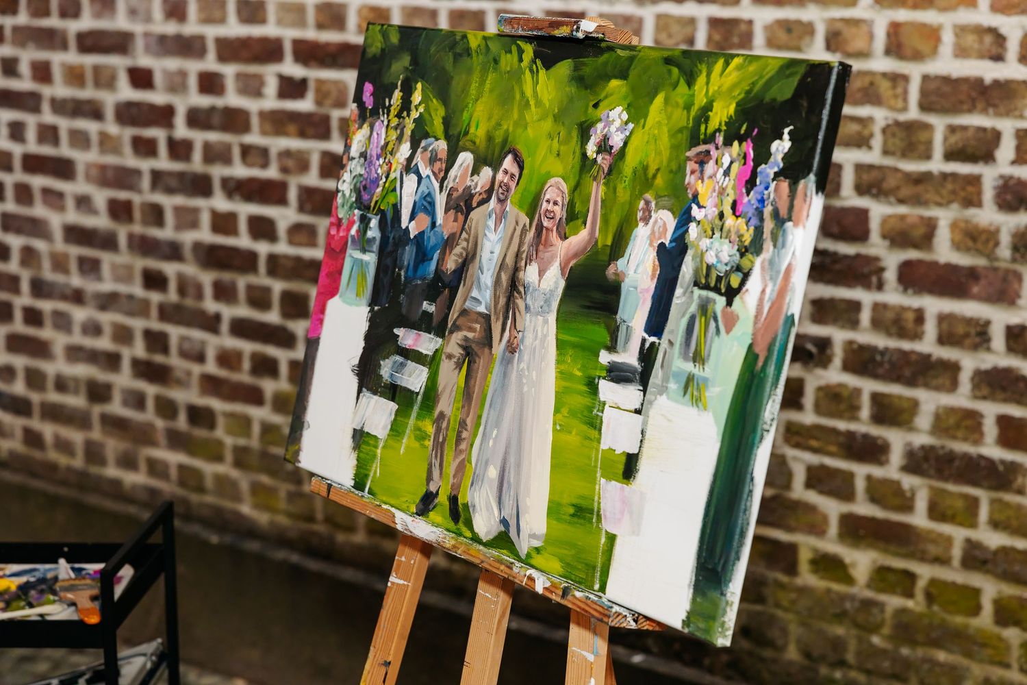 Live wedding painting on easel showing bride and groom celebrating at outdoor ceremony.