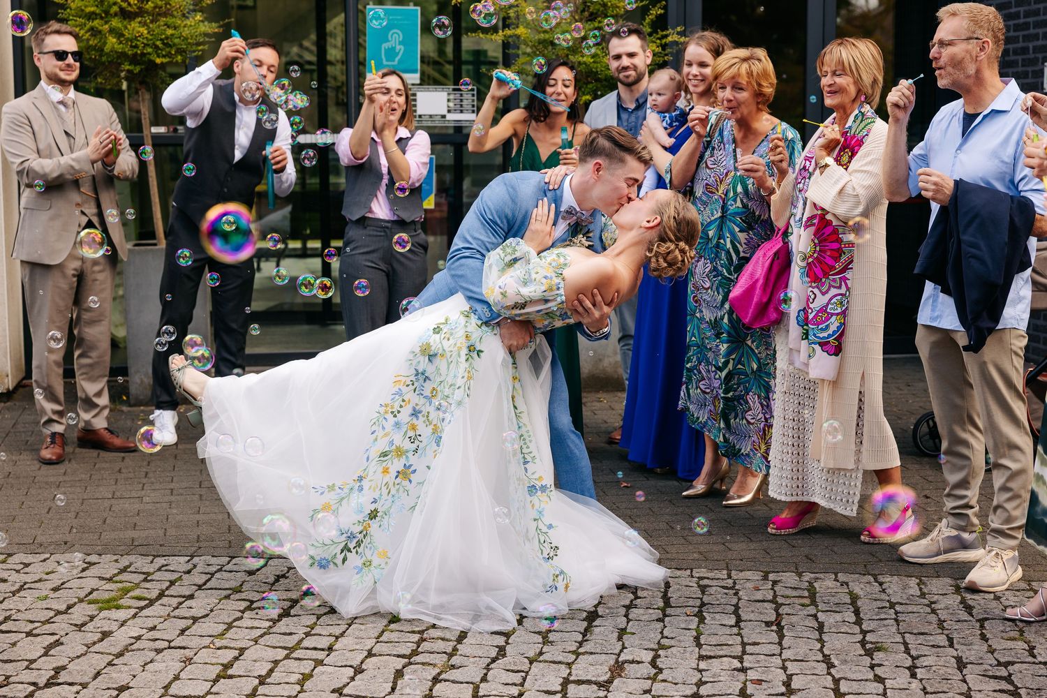 Bride and groom sharing a dip kiss surrounded by guests blowing bubbles.