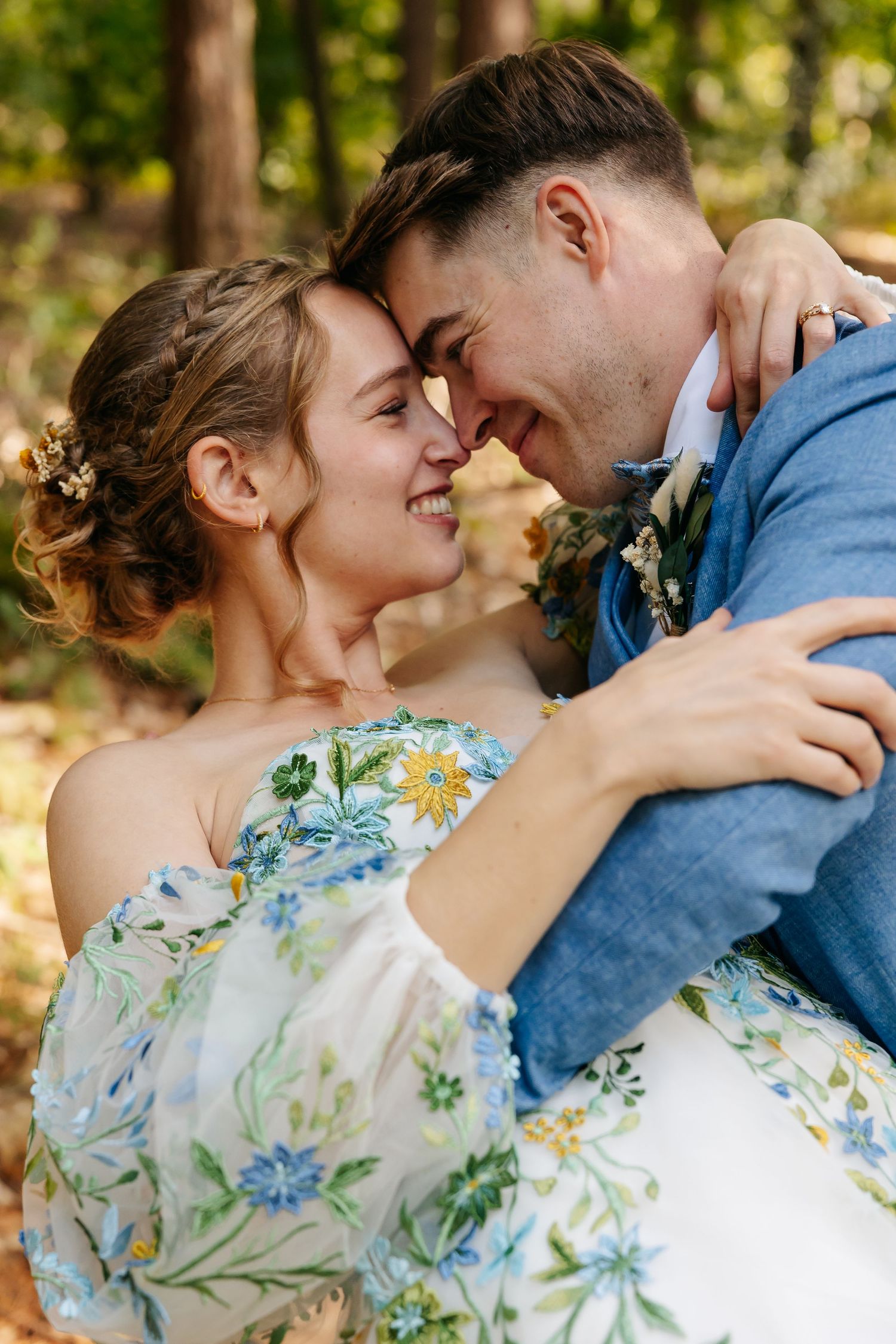 Bride and groom touching foreheads and embracing in autumn forest.