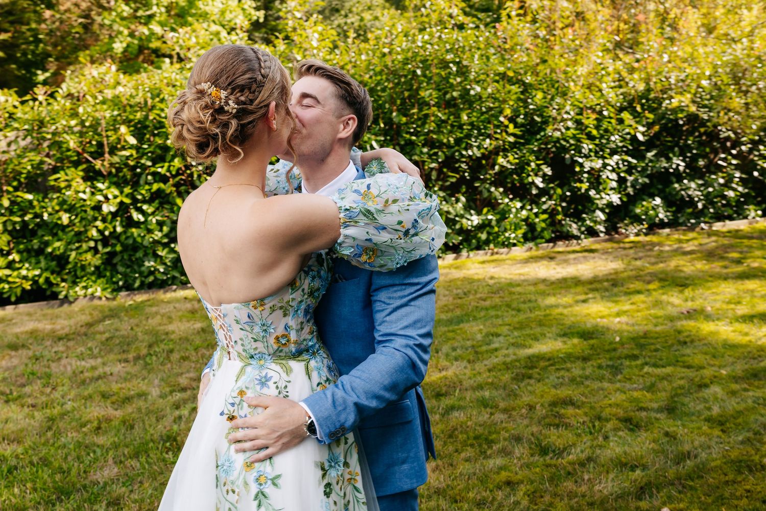 Groom in blue suit shares a tender kiss with bride in floral gown during outdoor wedding moment.