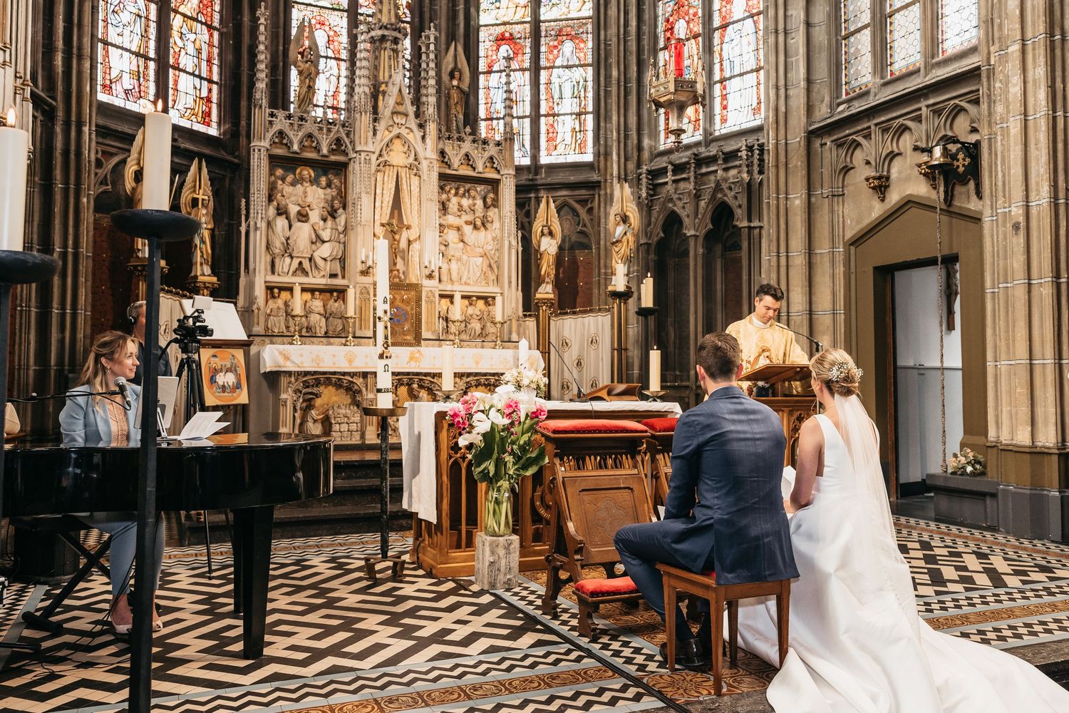 Bride and groom seated at the altar of an ornate Gothic church during their wedding ceremony.