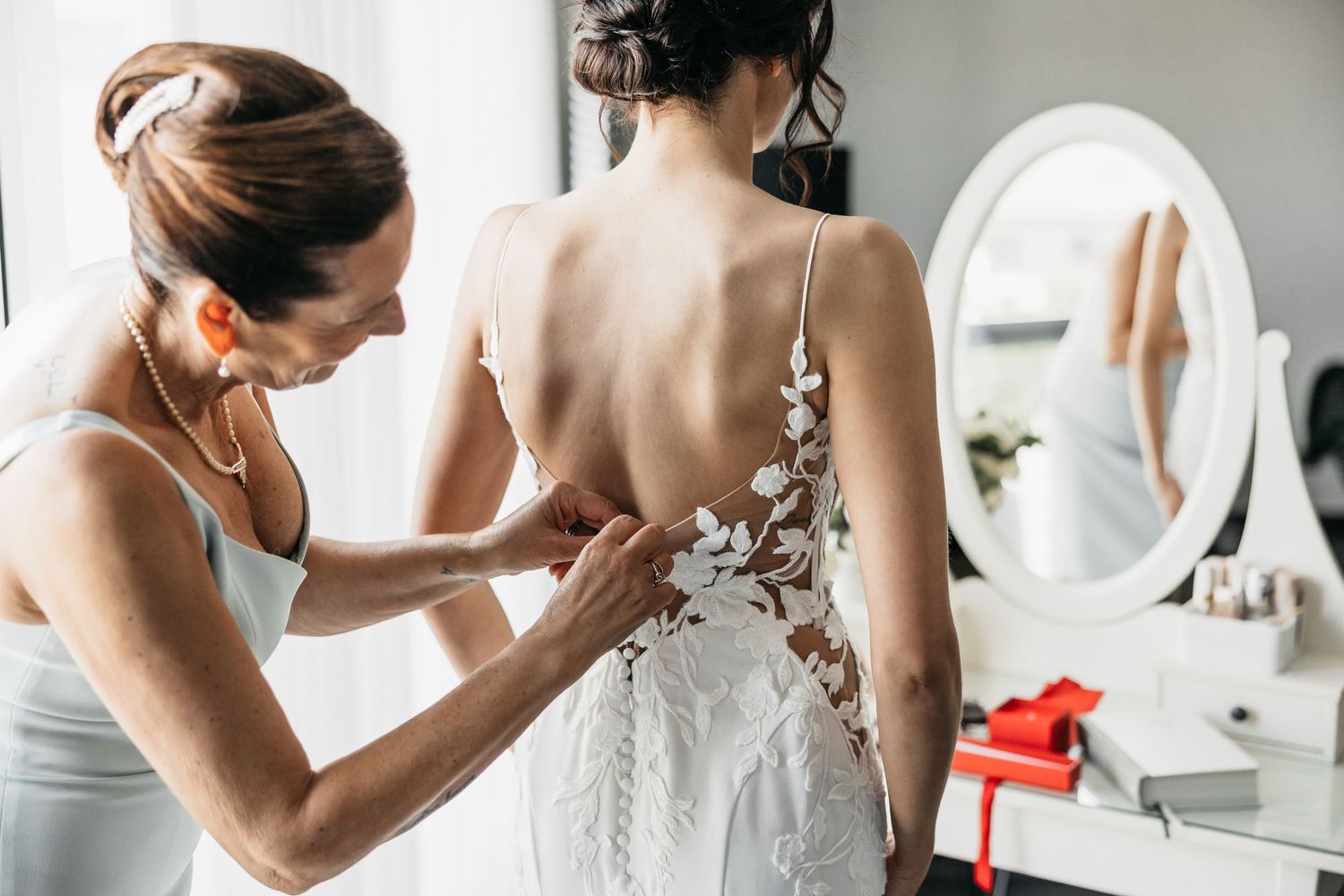 Close-up of mother fastening floral lace back of bride's wedding dress.