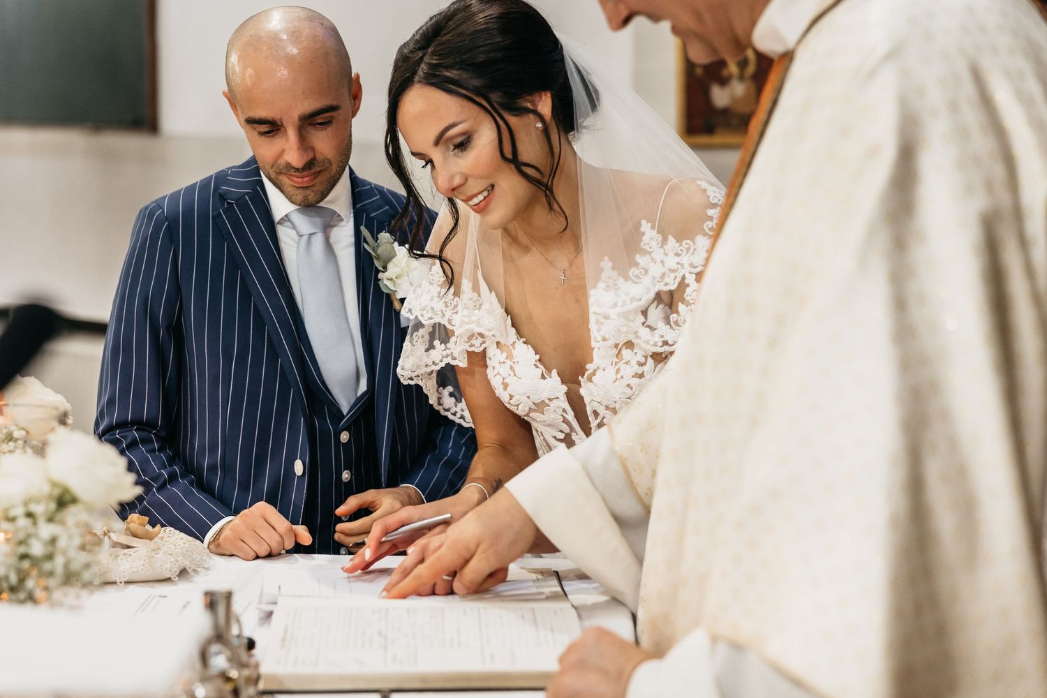 Bride and groom signing wedding register with officiant during church marriage ceremony.