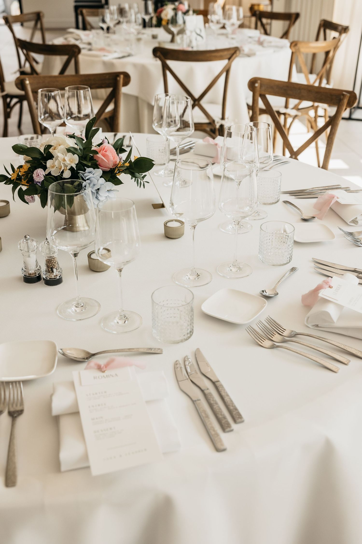 Close-up of wedding table setting with crystal glasses, silverware, pink flowers, and menu cards.