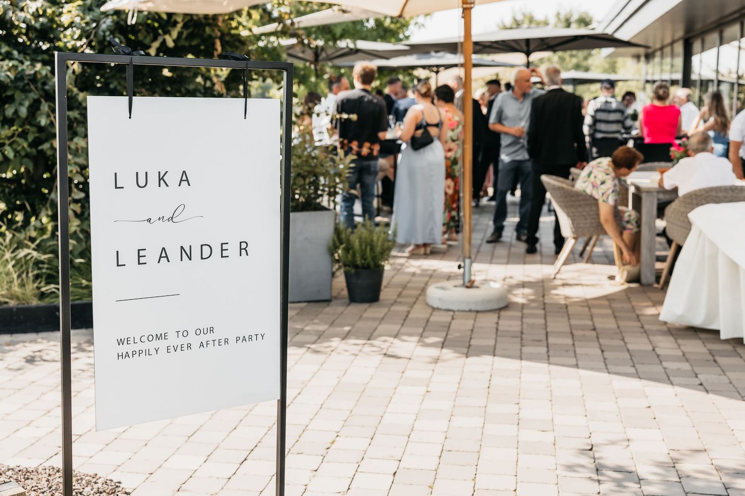 Wedding welcome sign reading Luka and Leander Happily Ever After Party on outdoor patio.