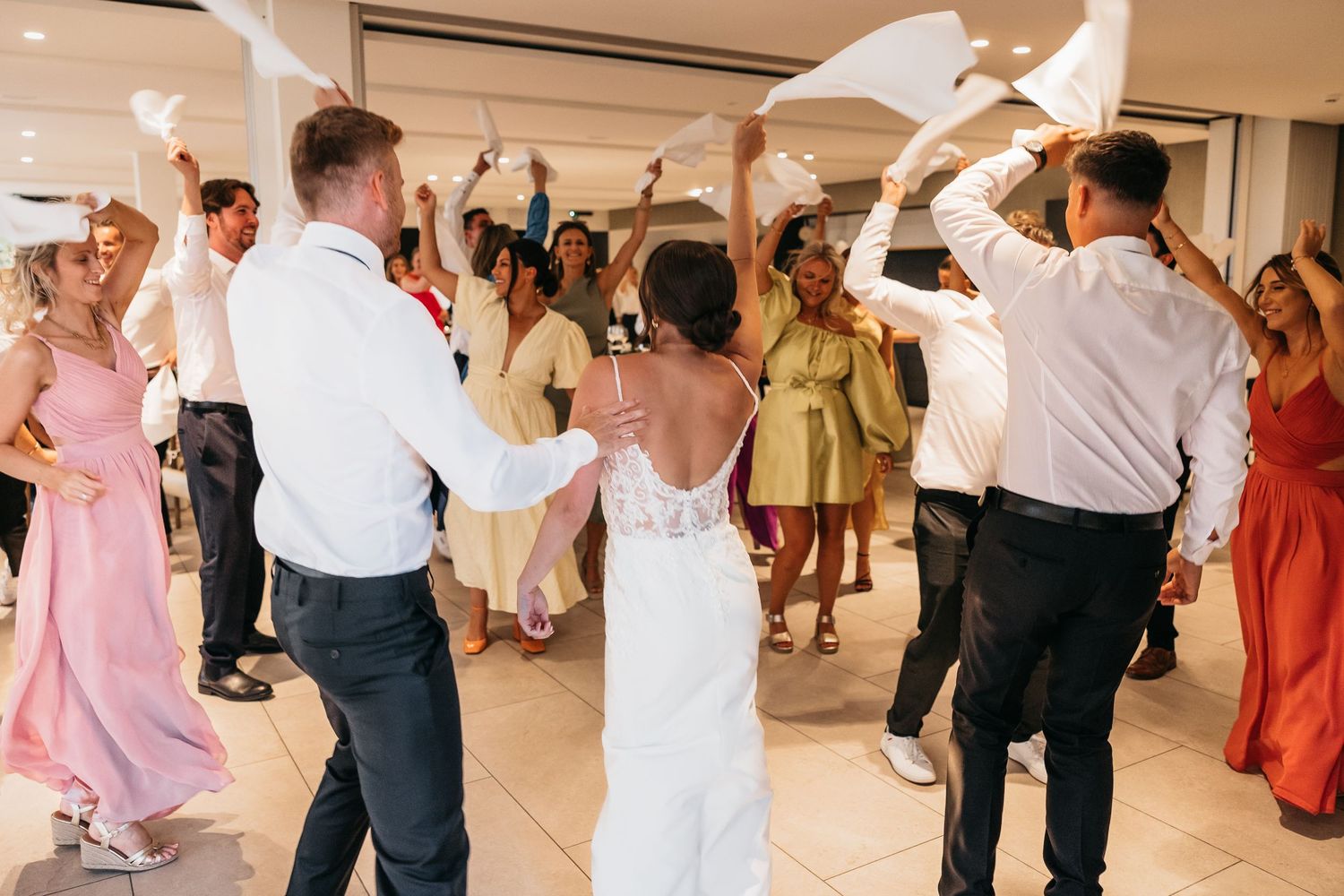 Wedding guests surround bride and groom waving napkins on dance floor.