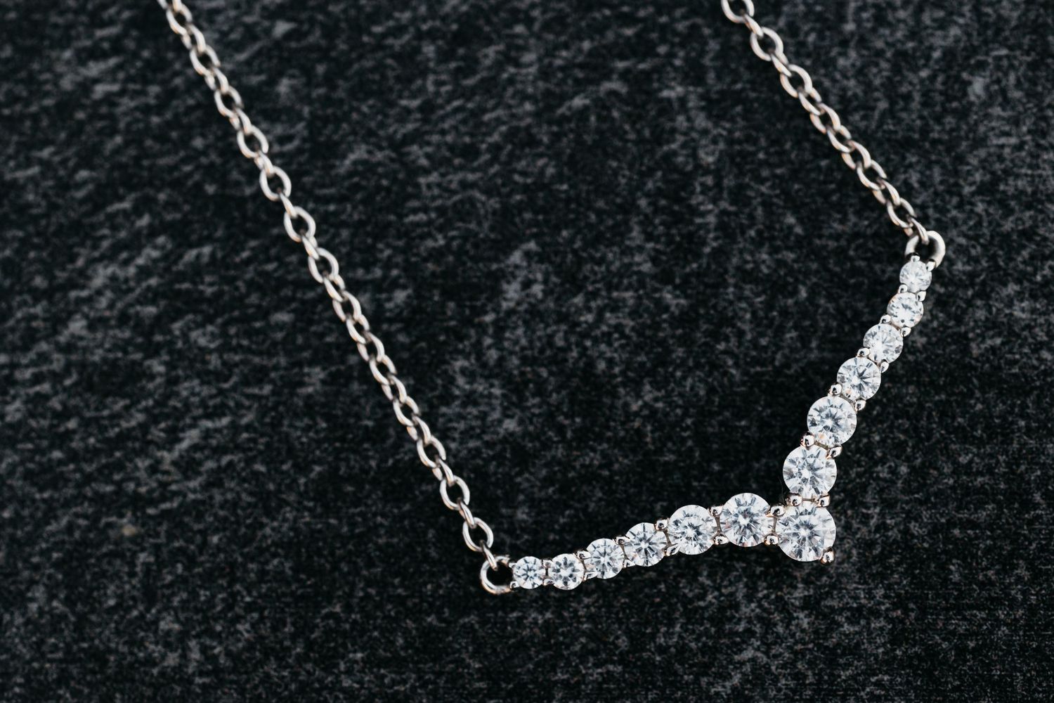 Delicate diamond V-shaped pendant necklace with sparkling stones on a fine chain against dark velvet.