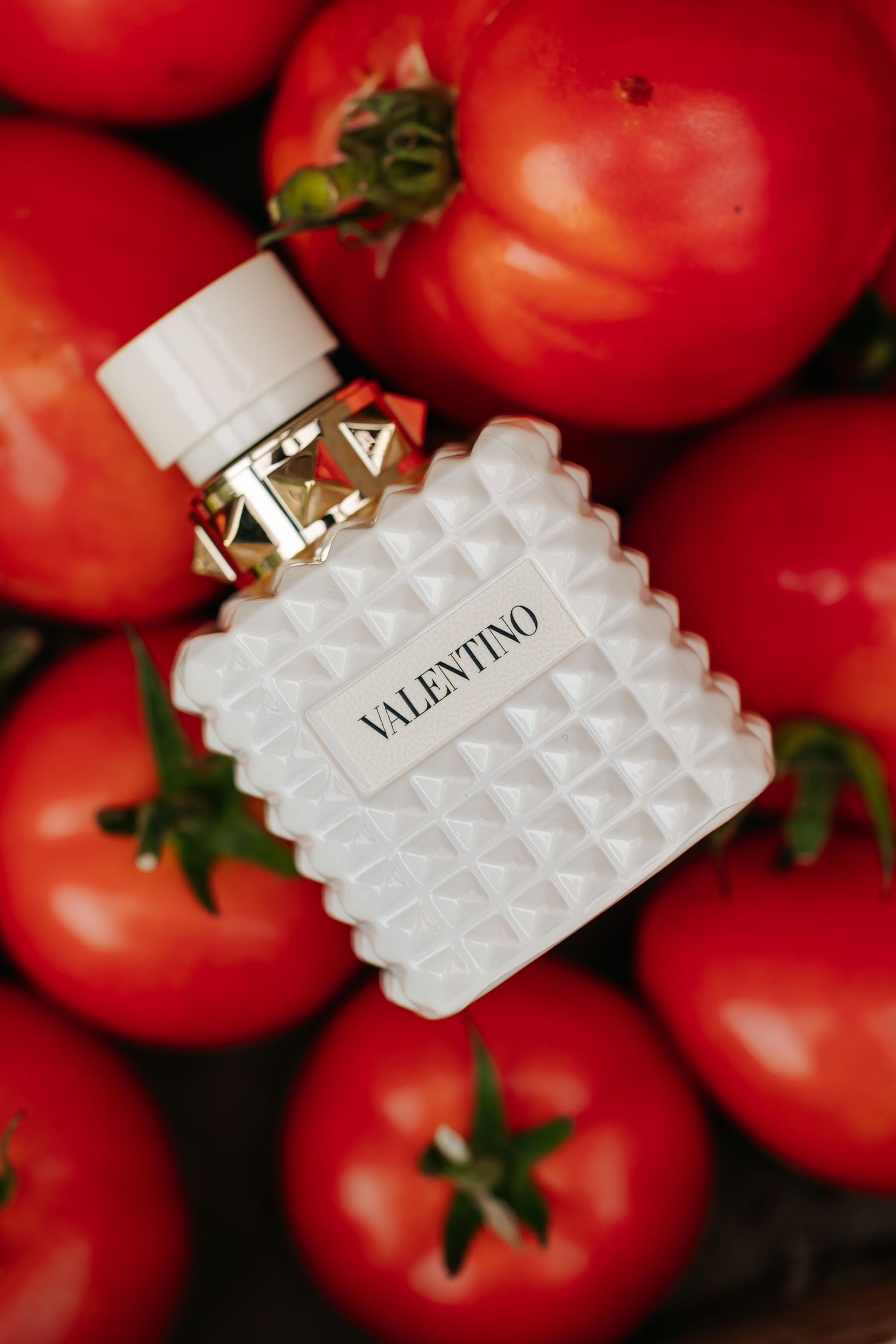 Valentino perfume bottle displayed elegantly surrounded by vibrant red tomatoes.