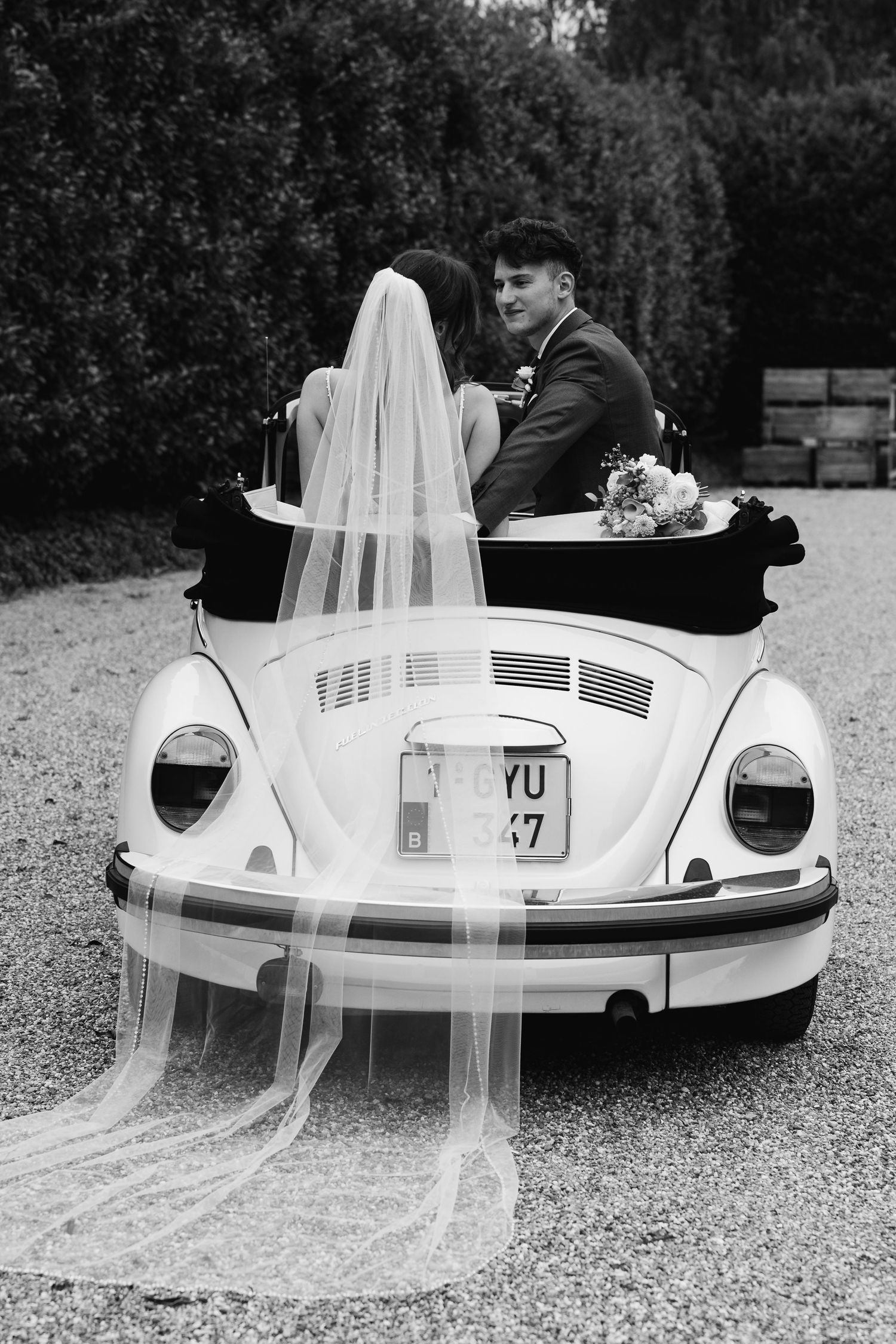 Black and white portrait of bride and groom seated in classic white VW Beetle convertible wedding car.