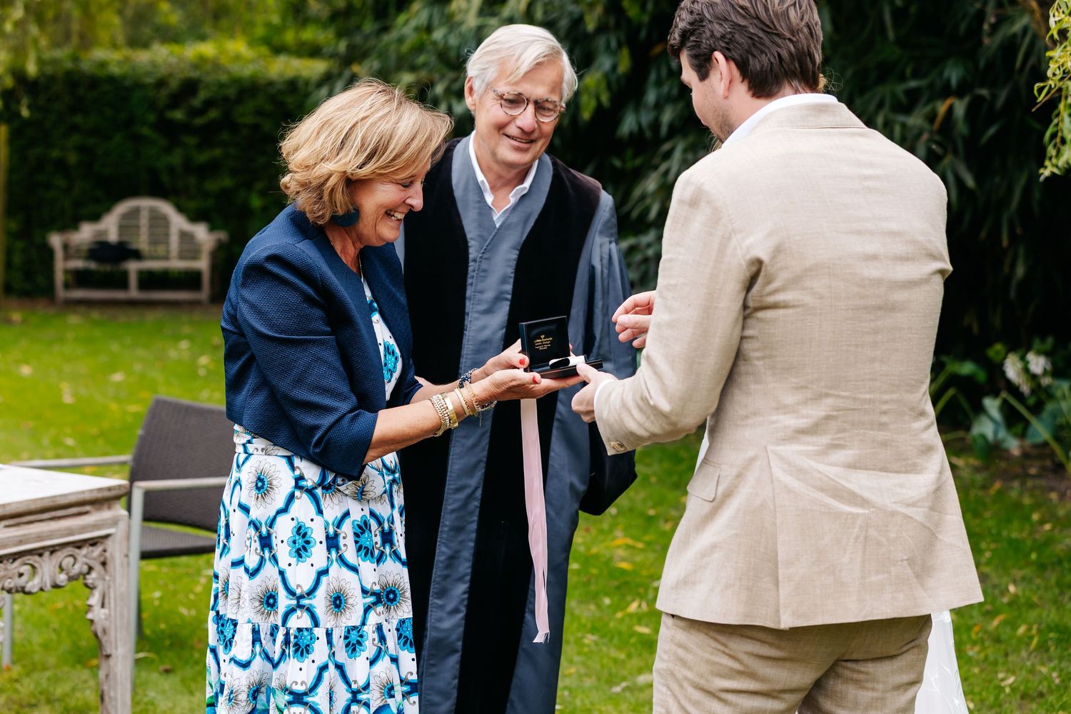Wedding officiant presenting ring box to groom during intimate outdoor garden ceremony.