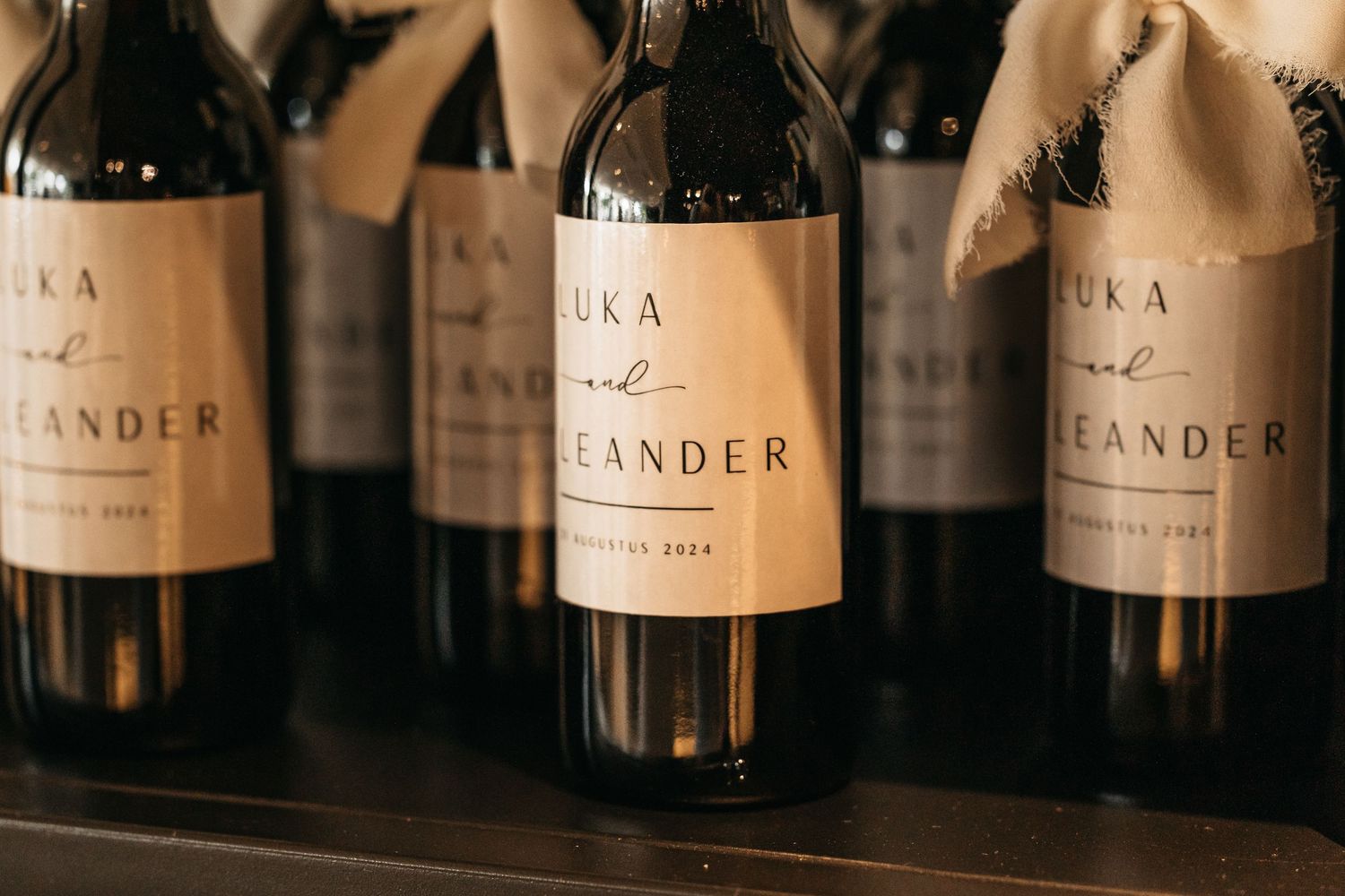 Row of personalized Luka and Leander wedding favor wine bottles displayed on a dark surface.