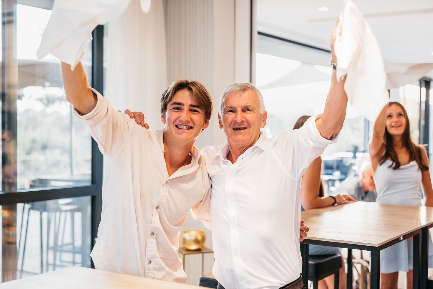 Two men smiling and waving white napkins in celebration at wedding.
