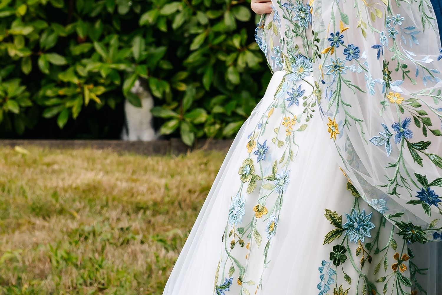 Close-up detail of a stunning white wedding gown with delicate blue and green floral embroidery.