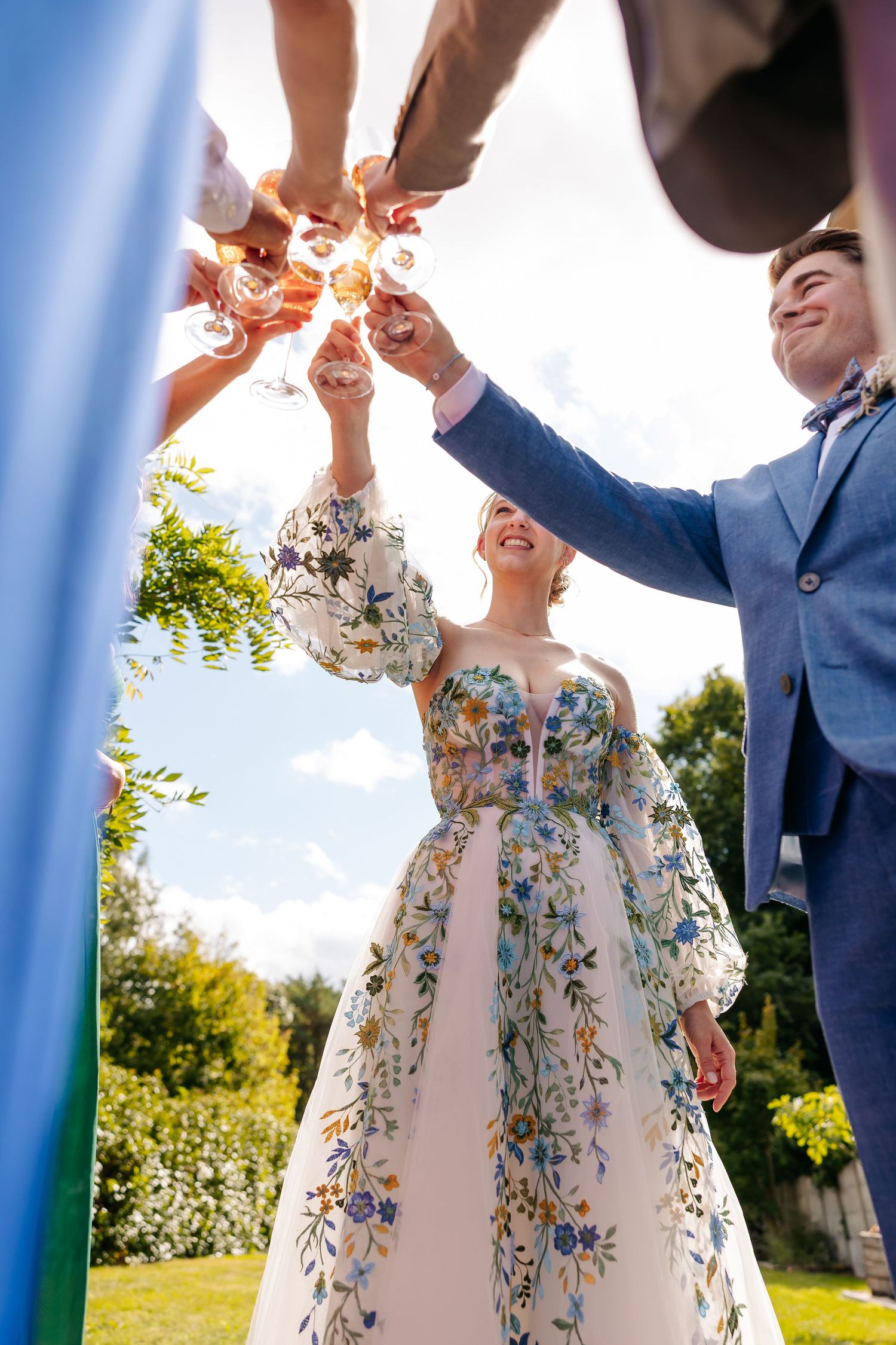 Wedding party toasting with champagne glasses raised outdoors on a sunny day.