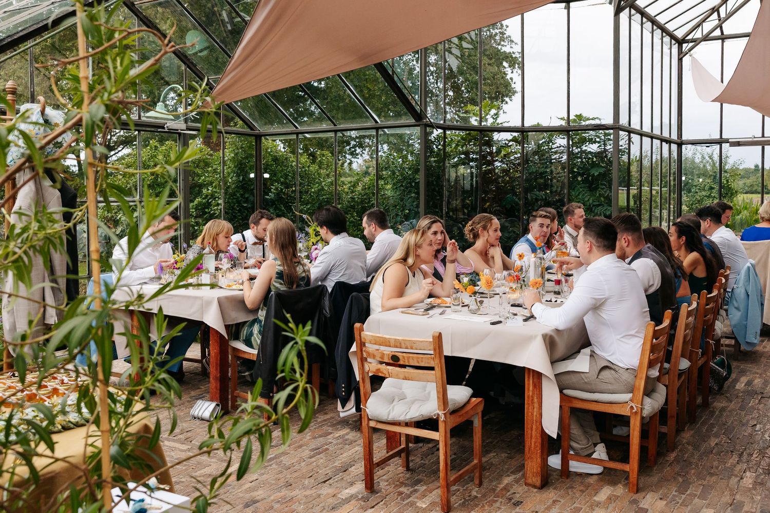 Wedding reception dinner in a beautiful greenhouse venue with guests seated at long decorated tables.
