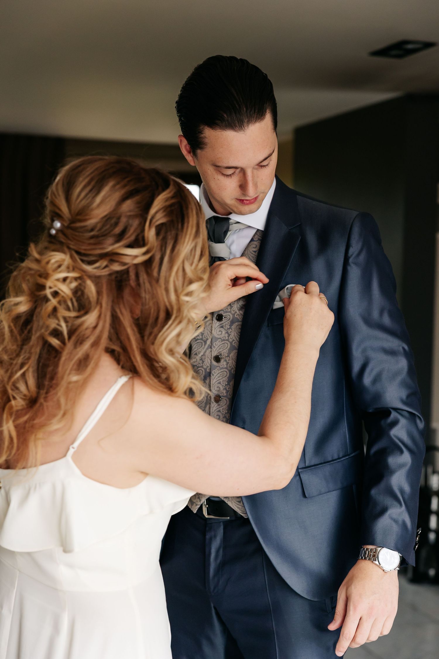 Bride adjusting groom's tie and pocket square as he looks down smiling.