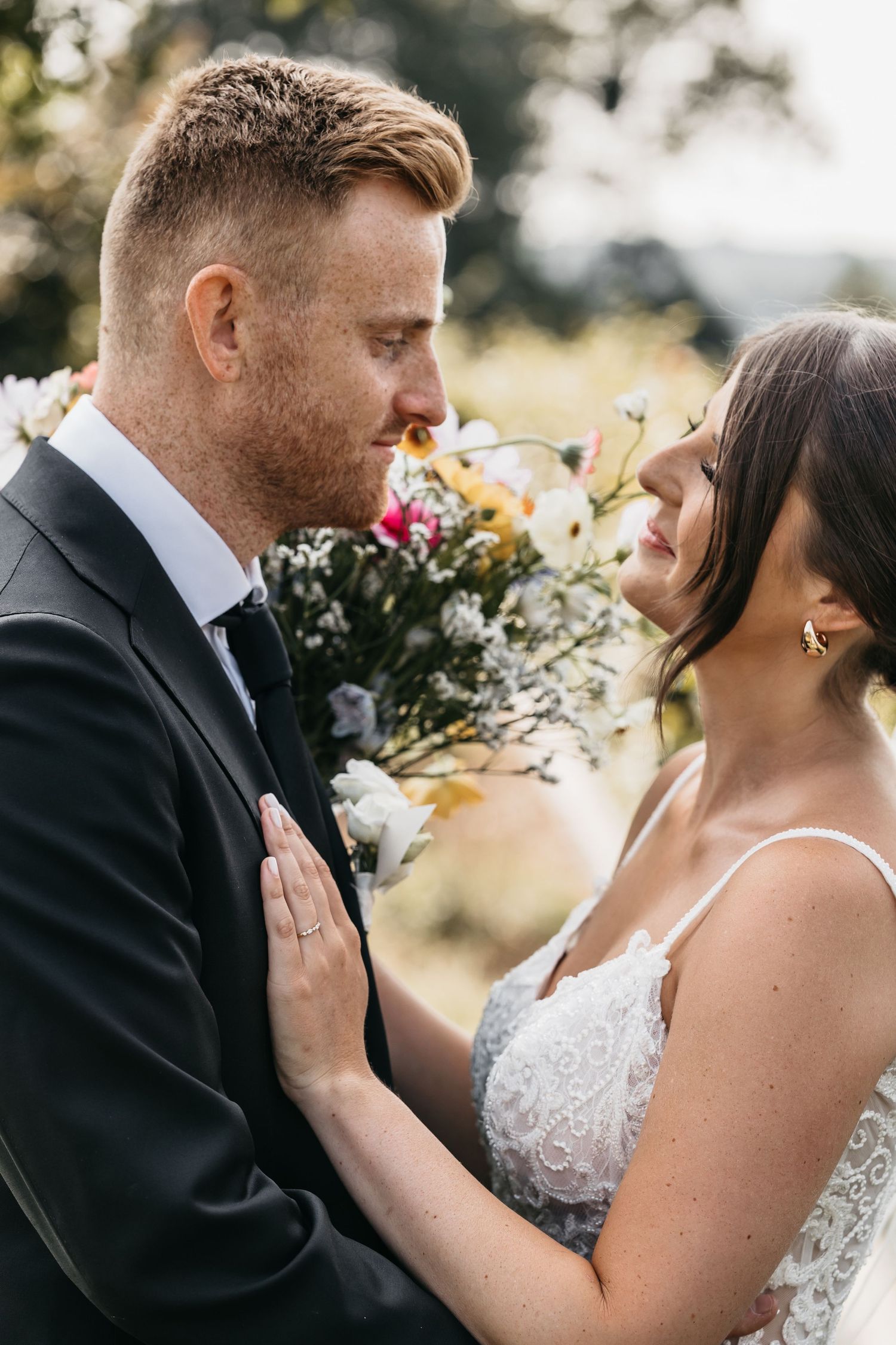 Bride and groom gazing into each others eyes, bride holding a colorful floral bouquet outdoors.