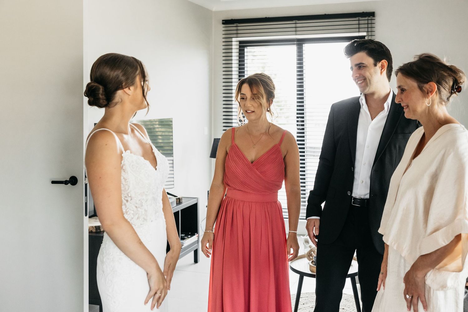 Bride sharing a joyful moment with smiling bridesmaids and family members during wedding morning prep.