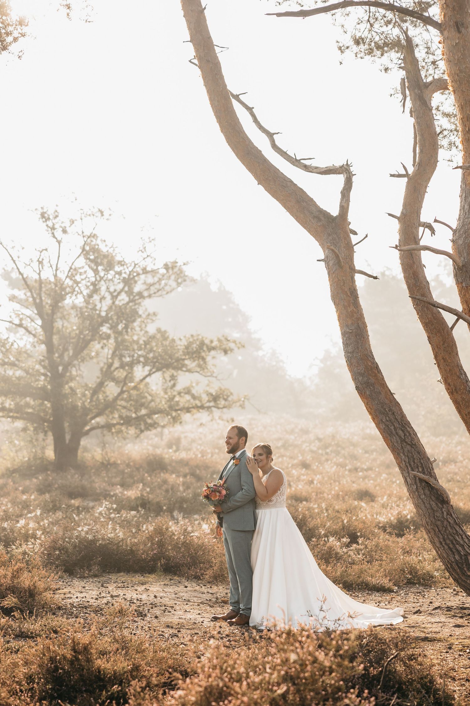 Bride and groom stand back-to-back in a misty forest clearing during their outdoor autumn wedding photo session.