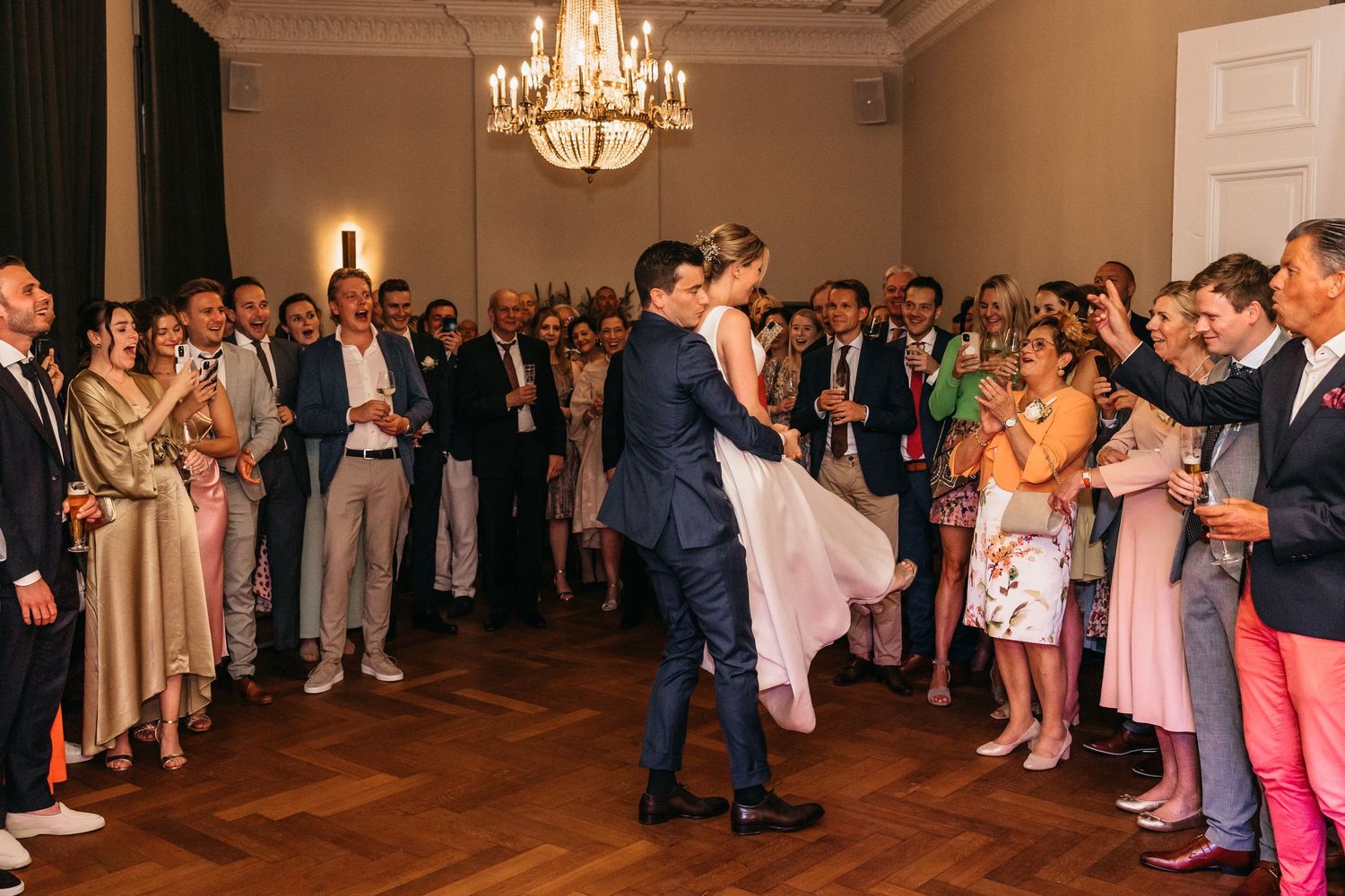 Newlyweds kissing during first dance surrounded by celebrating guests at reception.