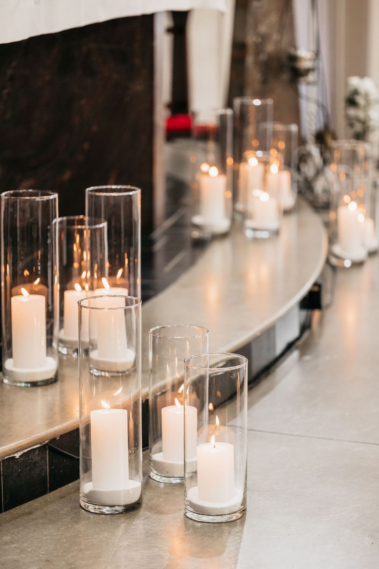 White pillar candles in glass cylinders arranged along church altar steps.