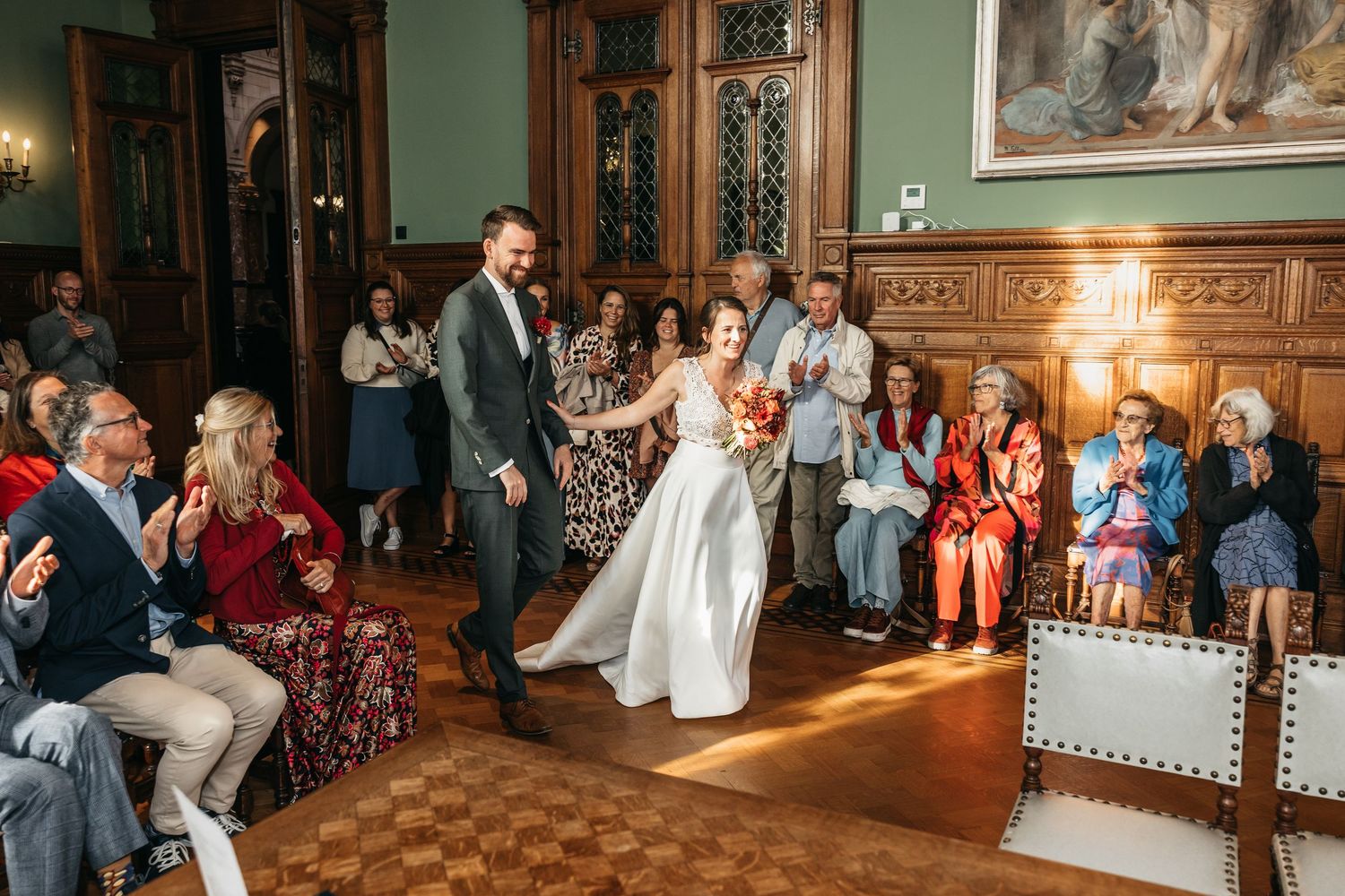 Bride and groom walking down the aisle at an elegant wood-paneled wedding ceremony hall with guests applauding.