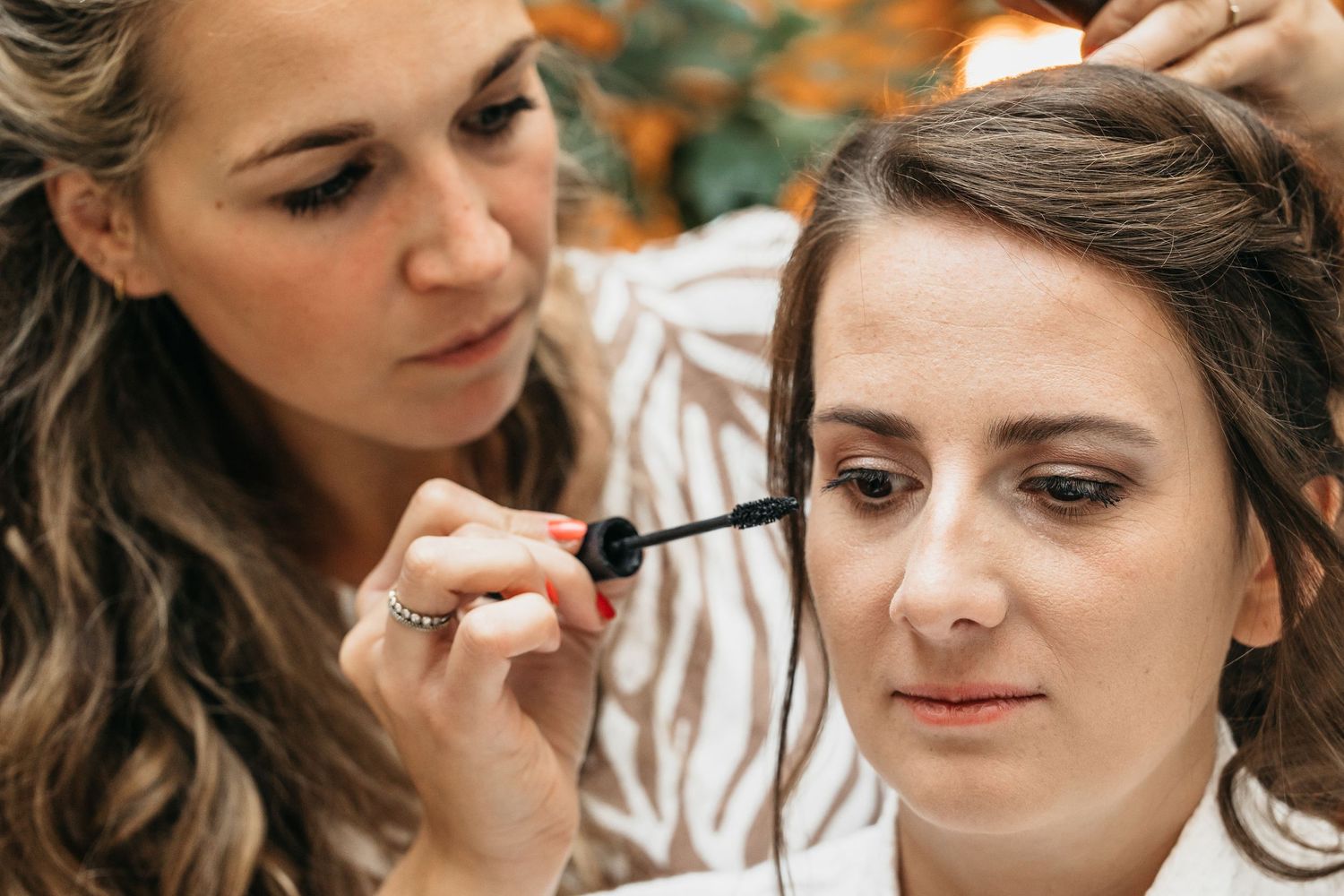 Makeup artist carefully applying mascara to a bride during wedding preparations.