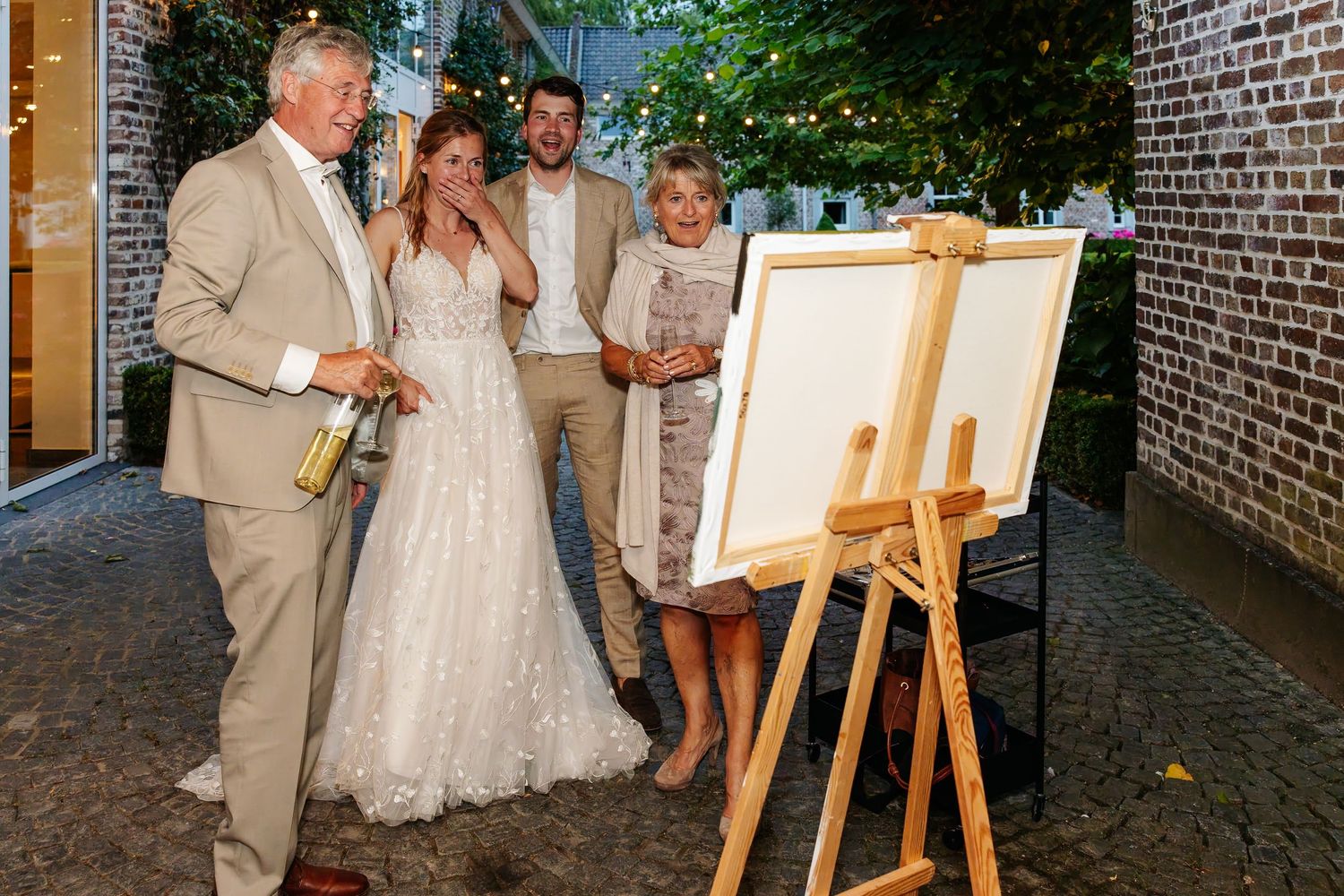 Wedding guests and couple gathered around a blank canvas on an easel at reception.
