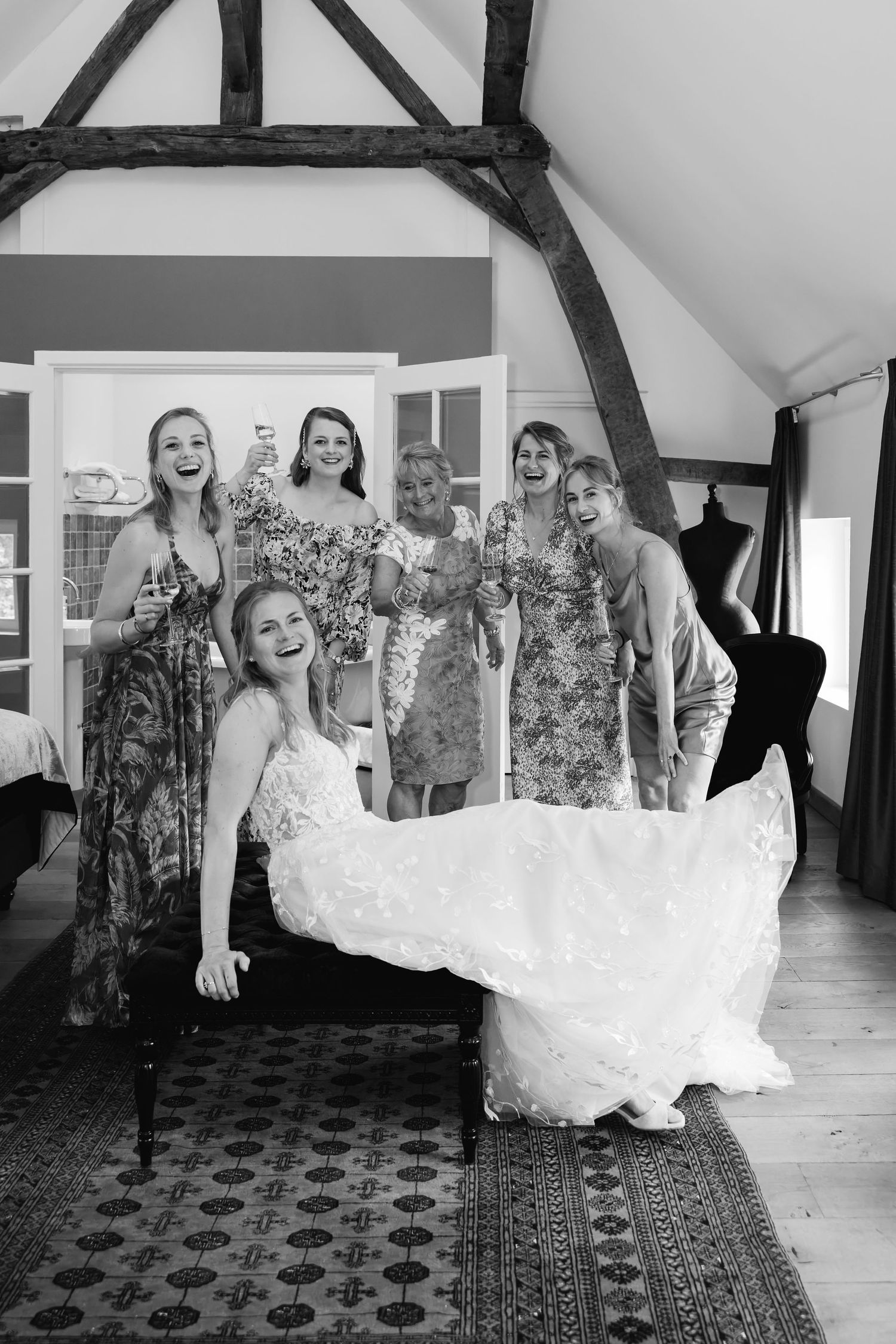 Bride laughing with bridesmaids in black and white wedding preparation photo inside rustic venue.