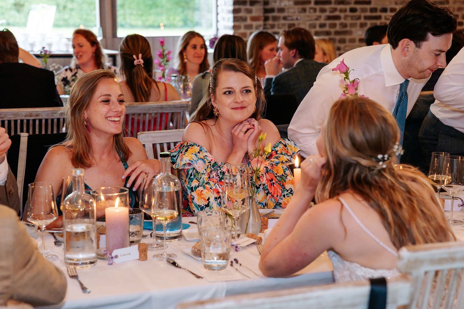 Smiling female wedding guests enjoying conversation at a candlelit reception dinner table.