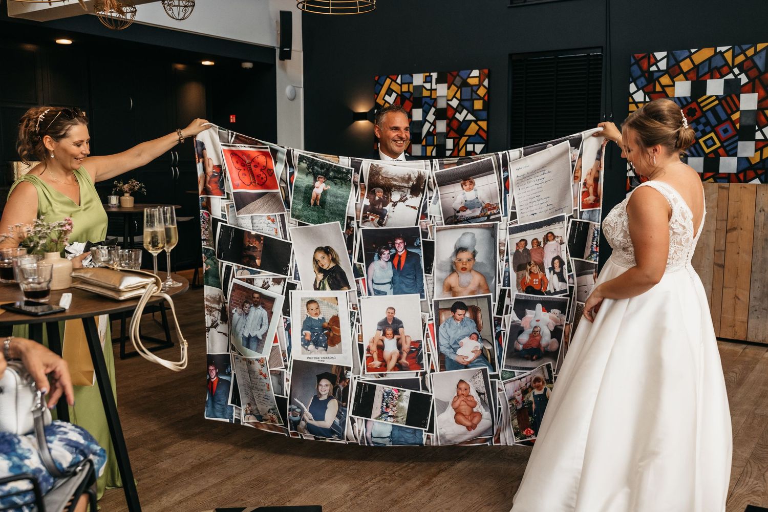 Bride and guests admiring a personalized photo collage blanket wedding gift at a colorful reception venue.