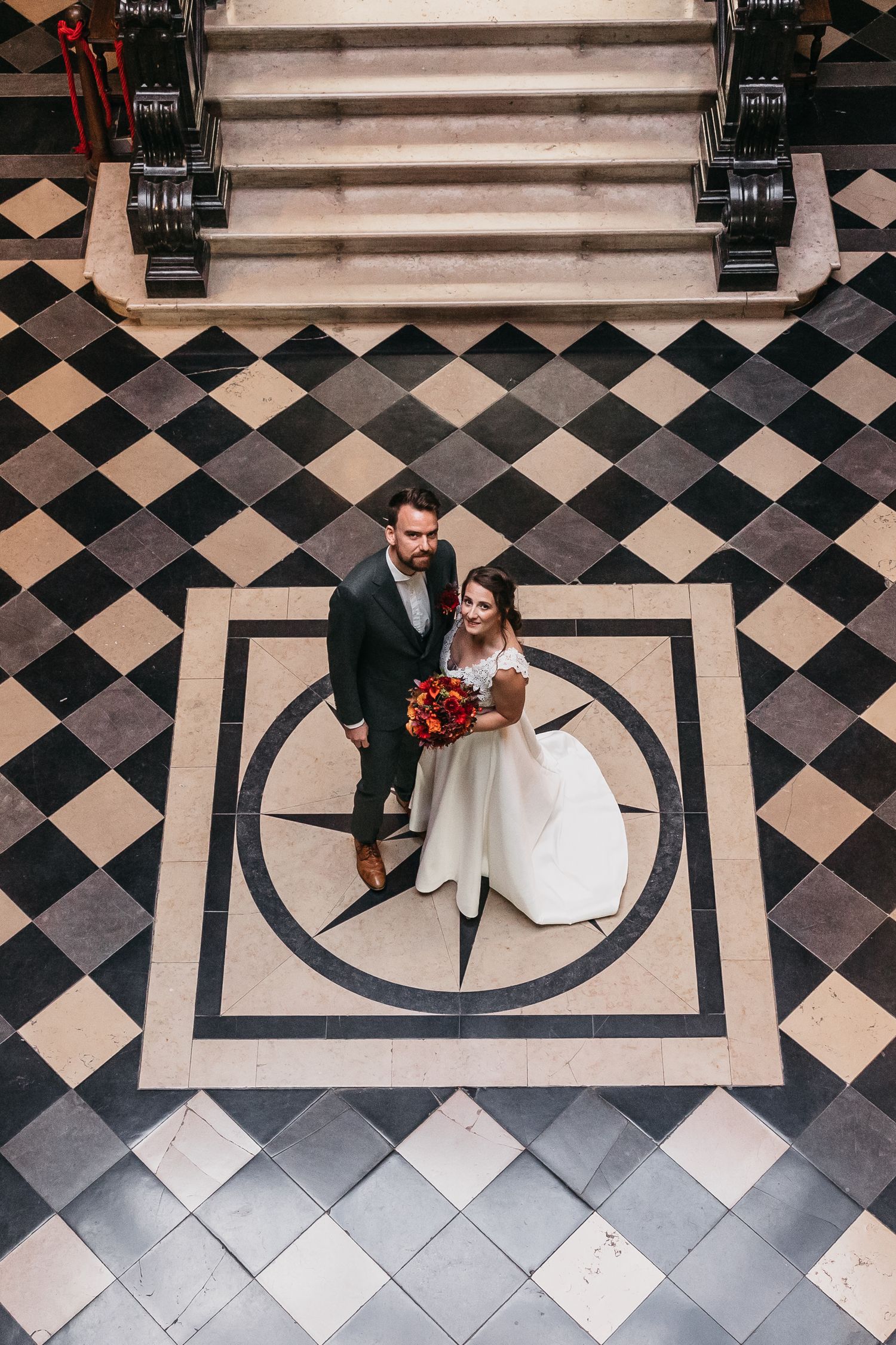 Aerial view of bride and groom standing on checkered marble floor.