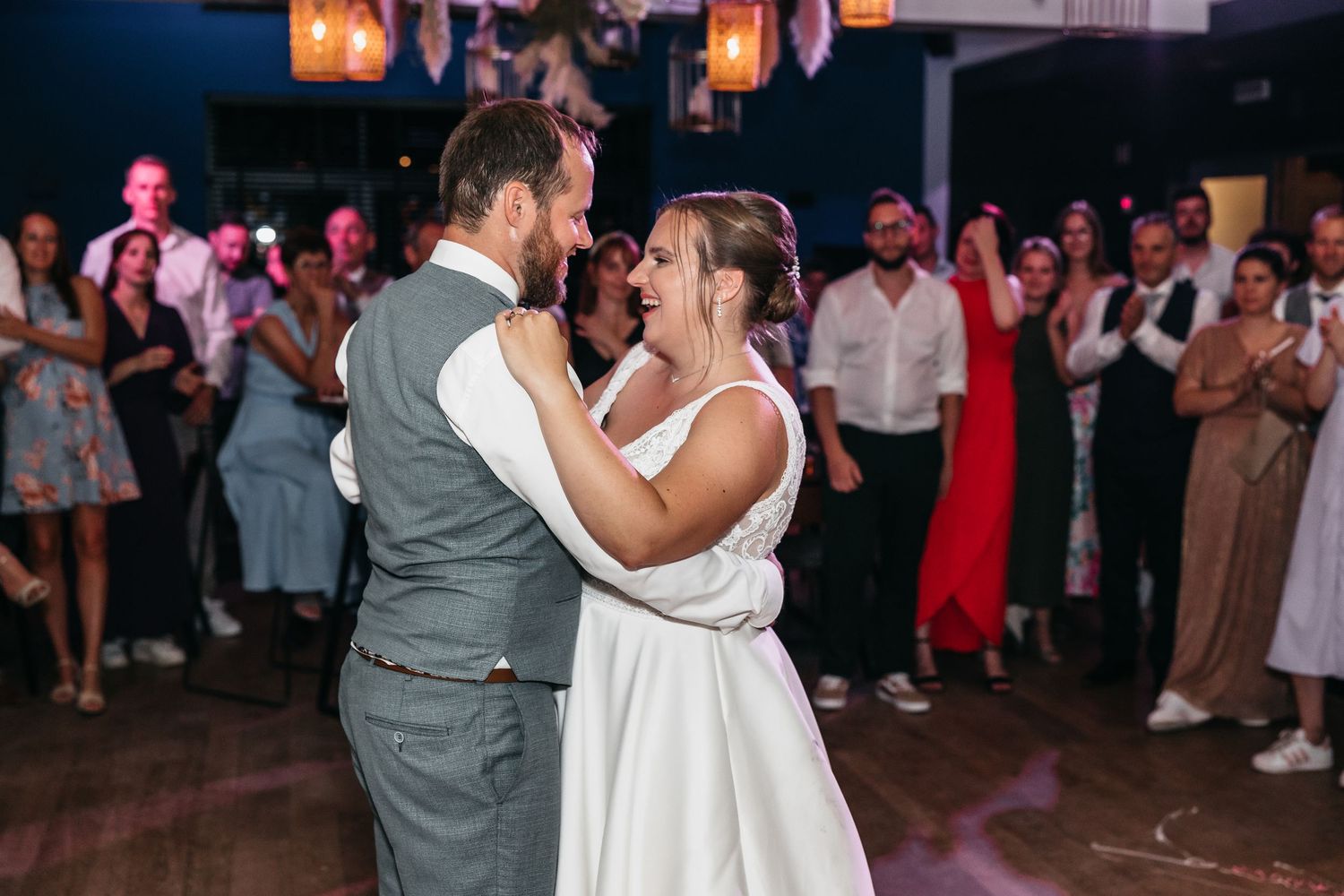 Bride laughs joyfully as she dances with her groom during their first dance surrounded by cheering wedding guests.
