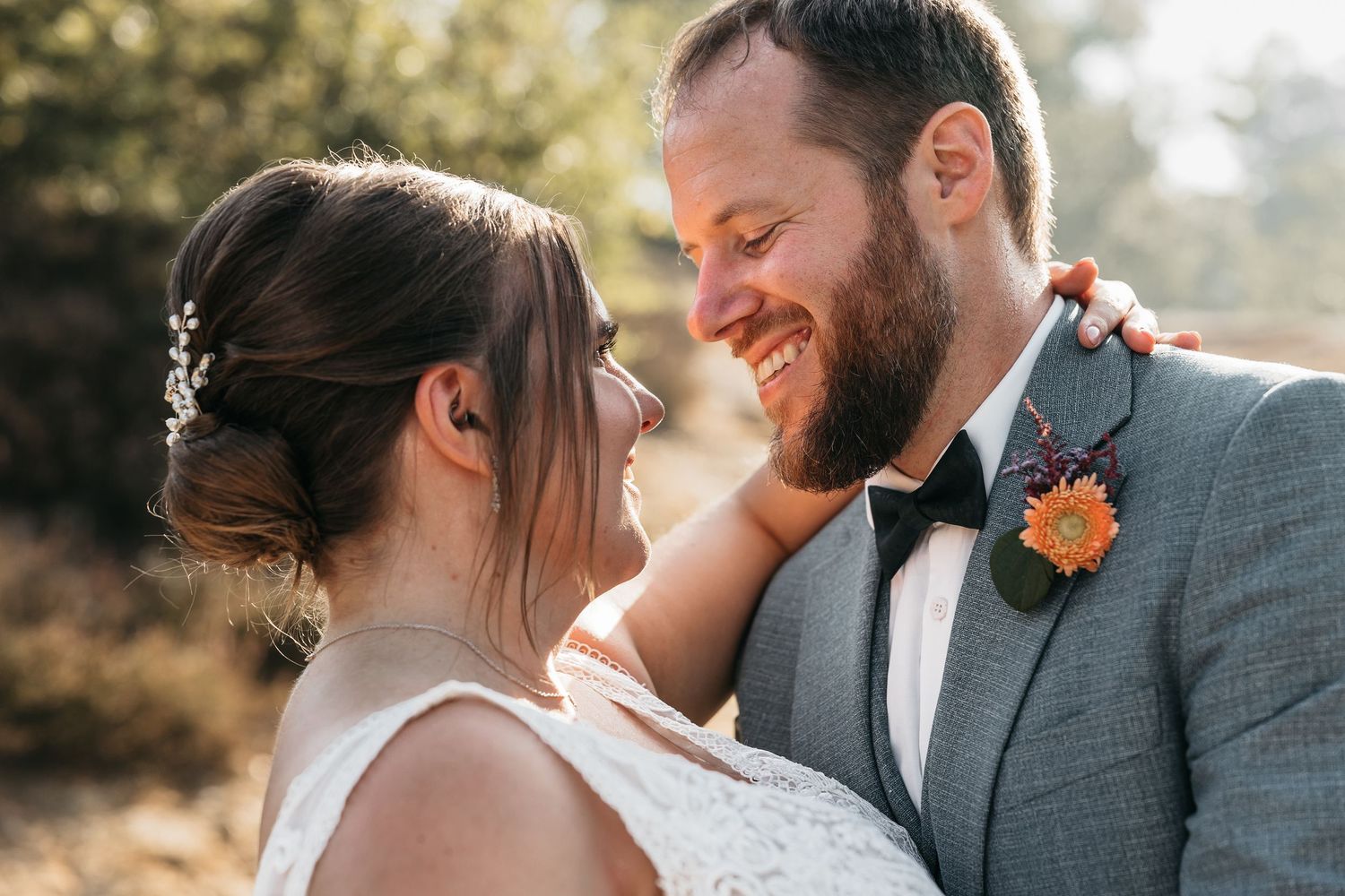 Joyful newlyweds smiling at each other closely with groom wearing a colorful floral boutonniere.