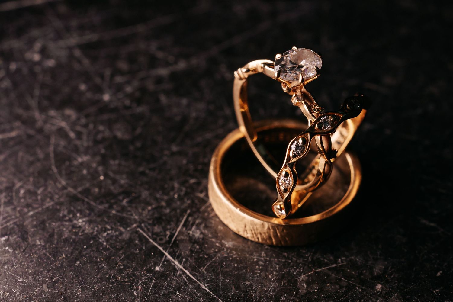 Elegant gold engagement and wedding rings stacked together on a dark textured surface.