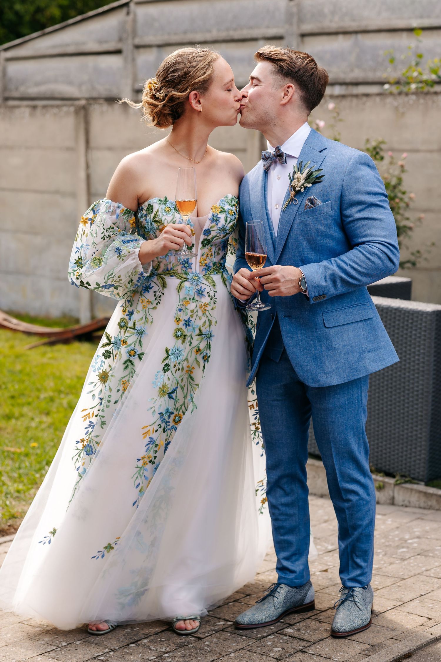 Bride and groom sharing a kiss while holding champagne glasses outdoors.