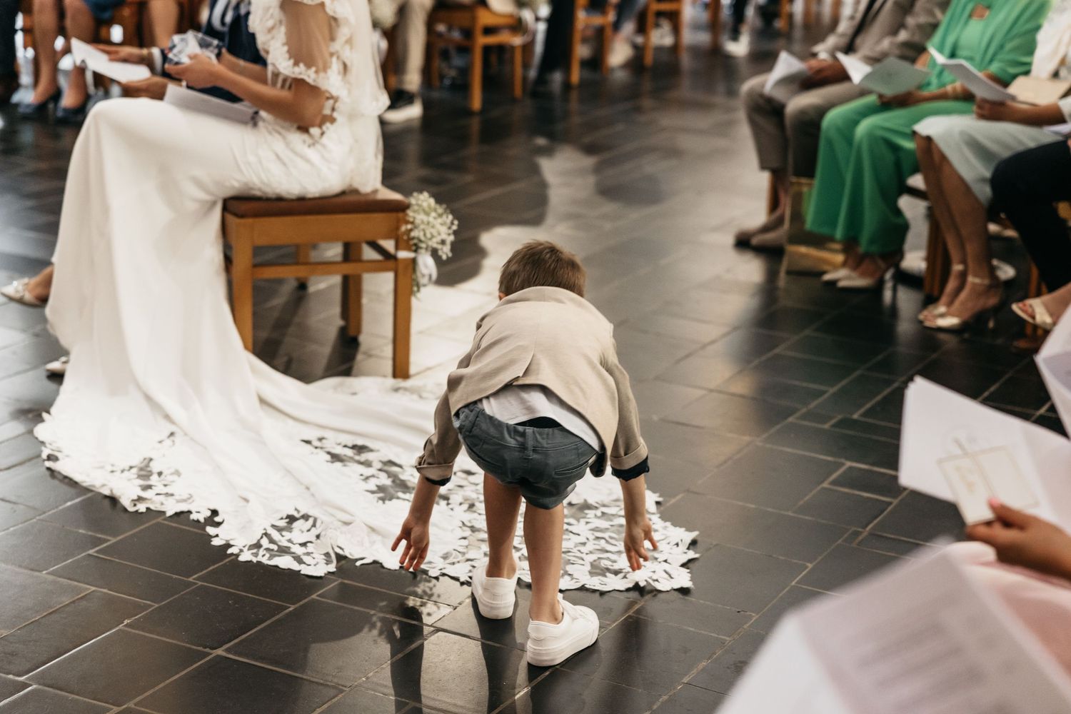 Young child crawling on church floor near bride's lace wedding dress train during ceremony.