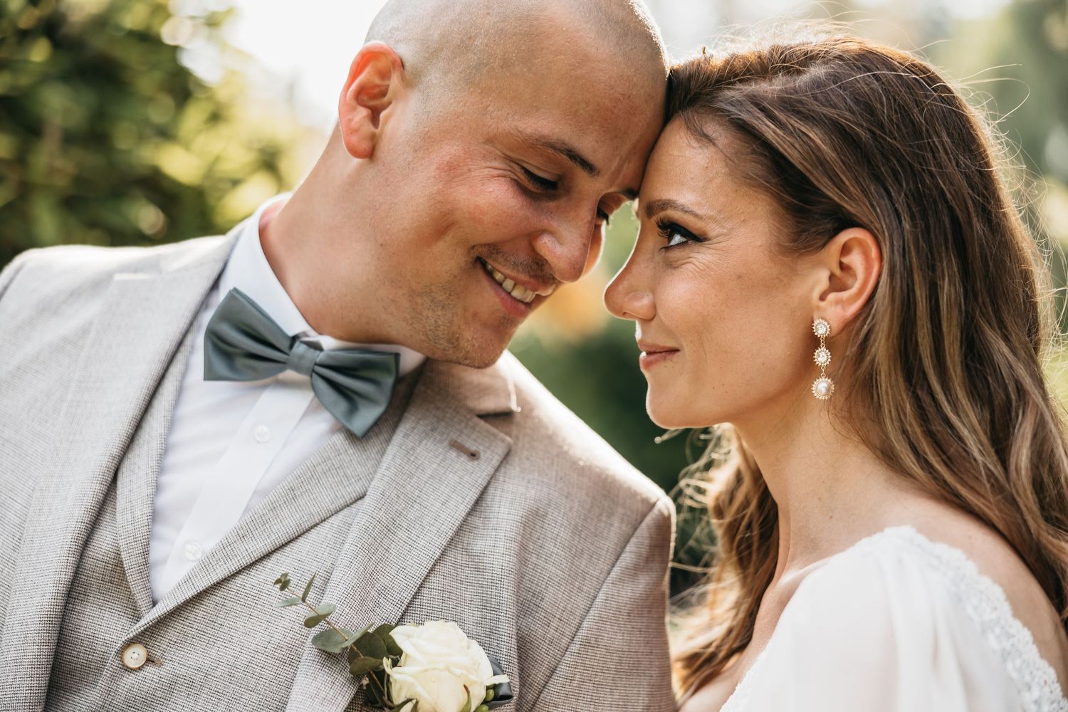 Bride and groom touching foreheads and smiling intimately in a close romantic wedding portrait.