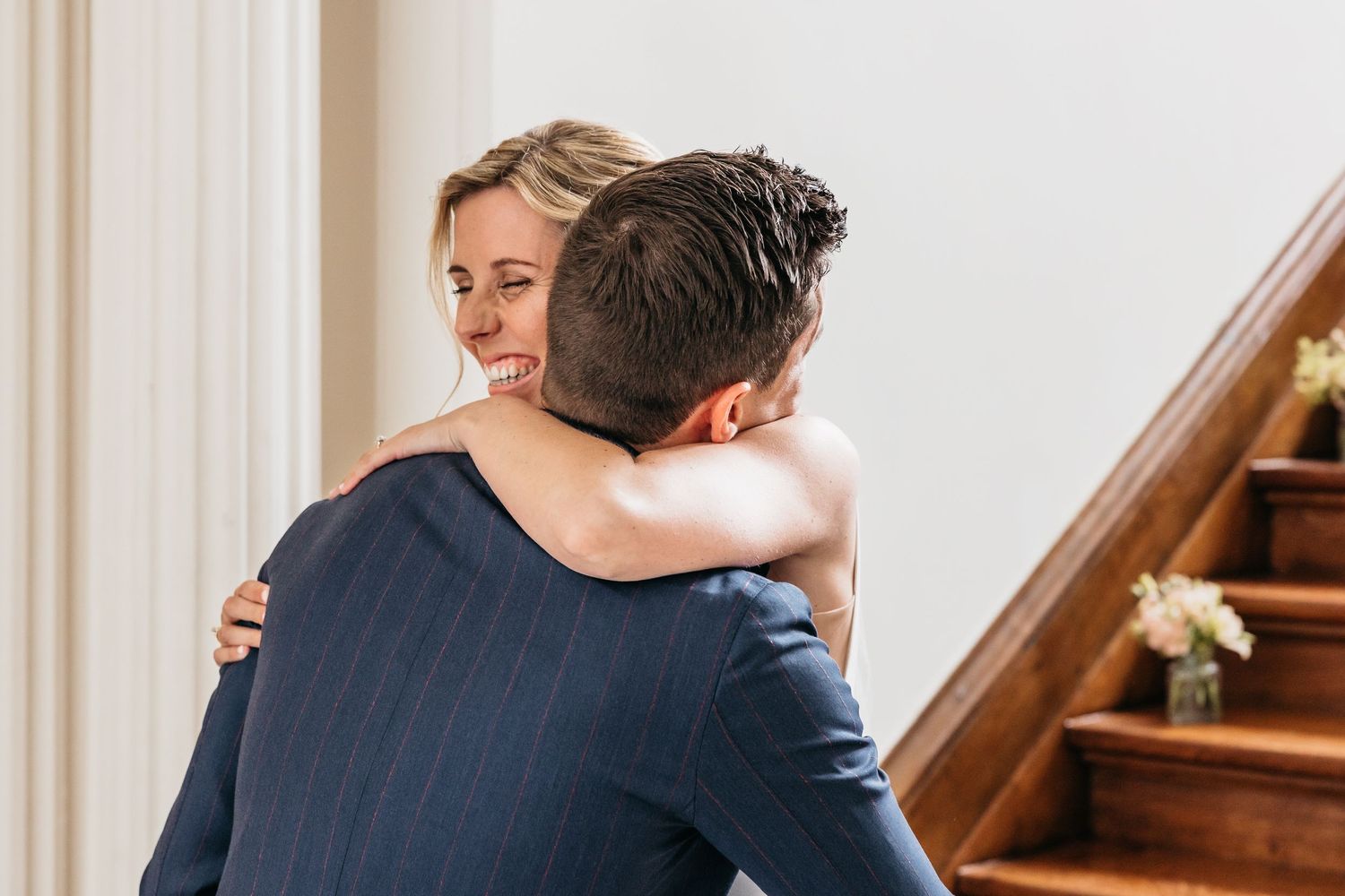 Bride and groom sharing emotional first look hug at bottom of wooden staircase.