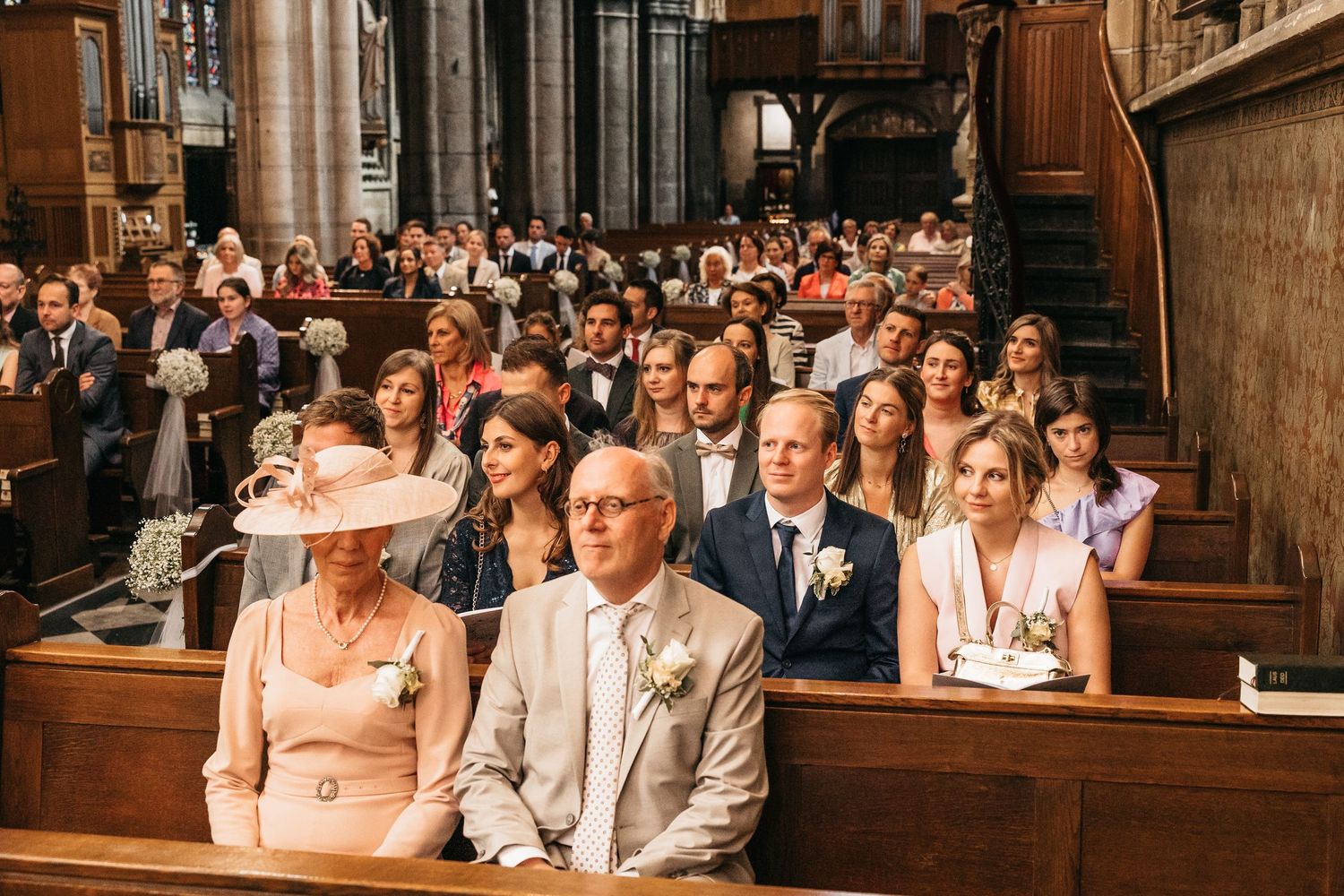 Wedding guests seated in church pews including elegantly dressed family members during ceremony.