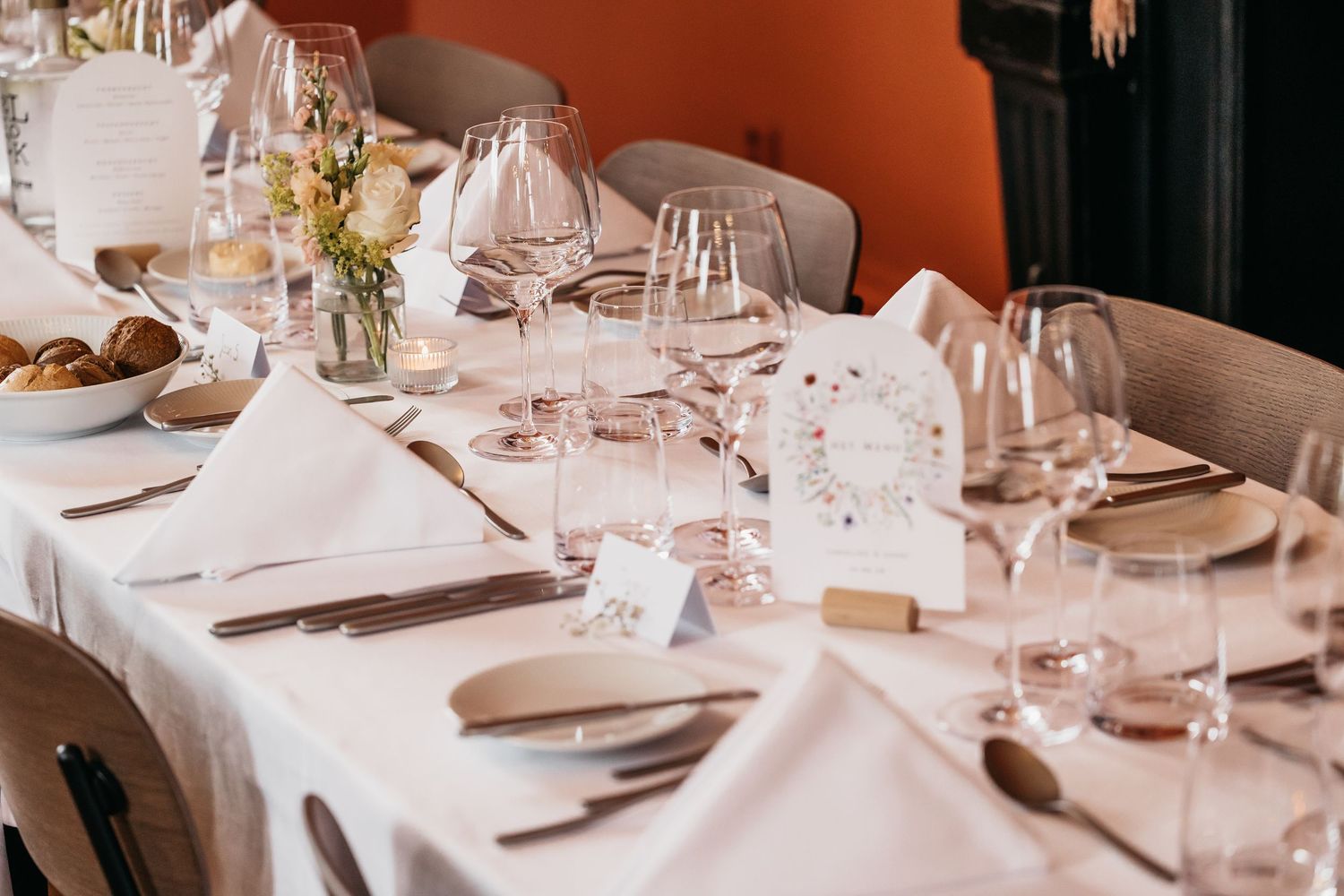 Elegant wedding reception table setting with white linens, crystal glasses, napkins, and floral menu cards.