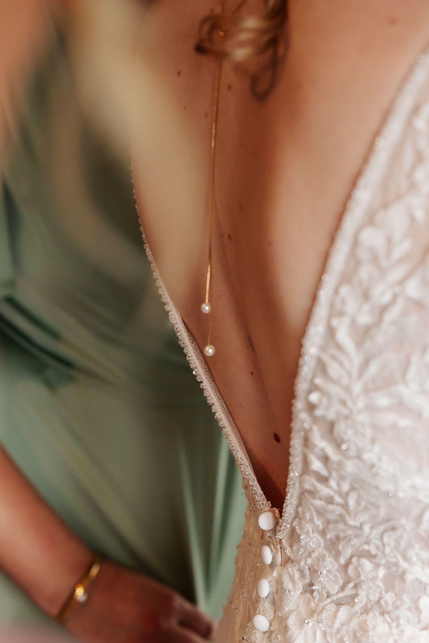 Close-up of a delicate gold back necklace with pearl drops against a lace backless bridal gown.