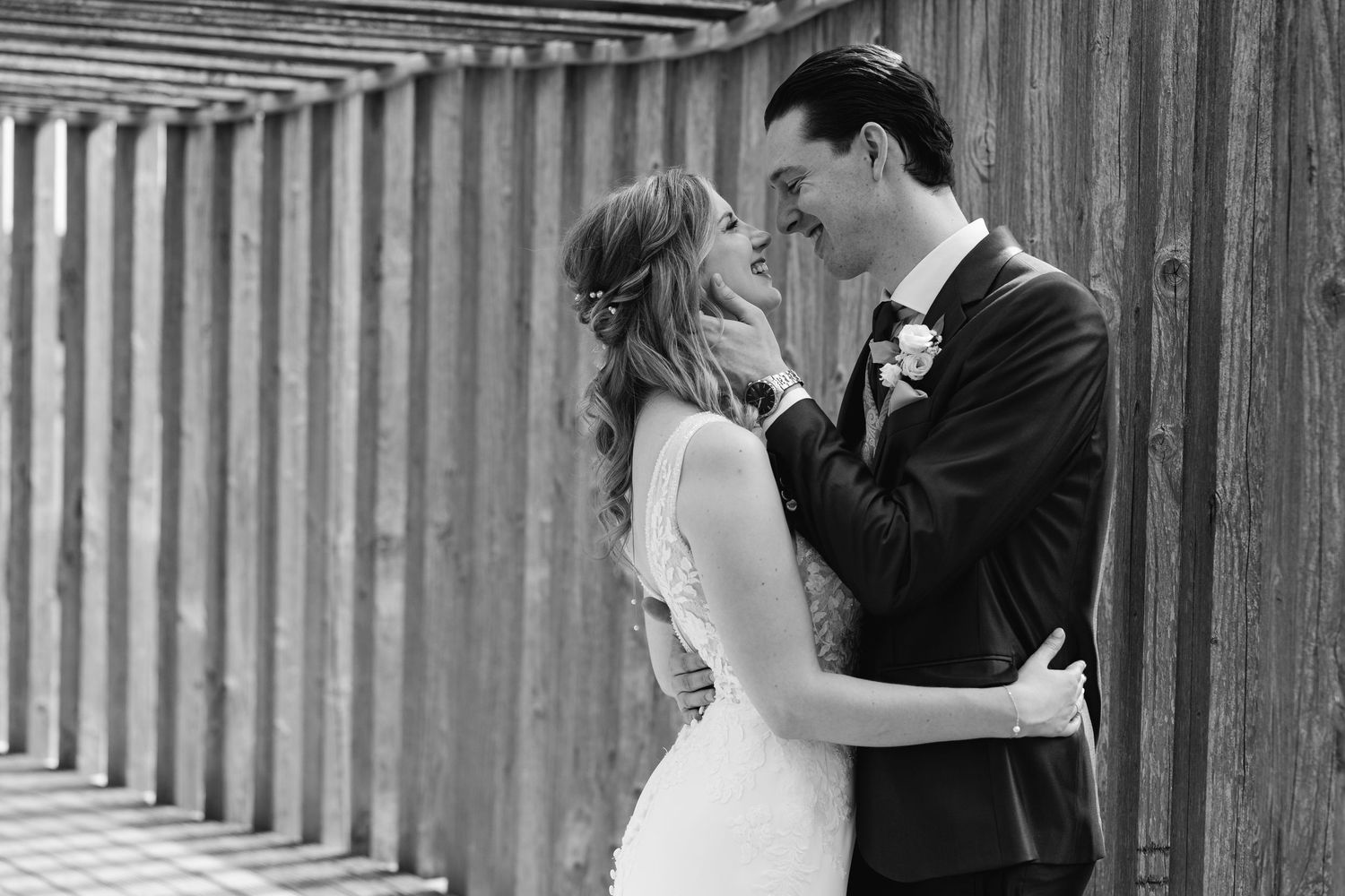 Black and white close-up of bride and groom almost kissing against wooden fence.