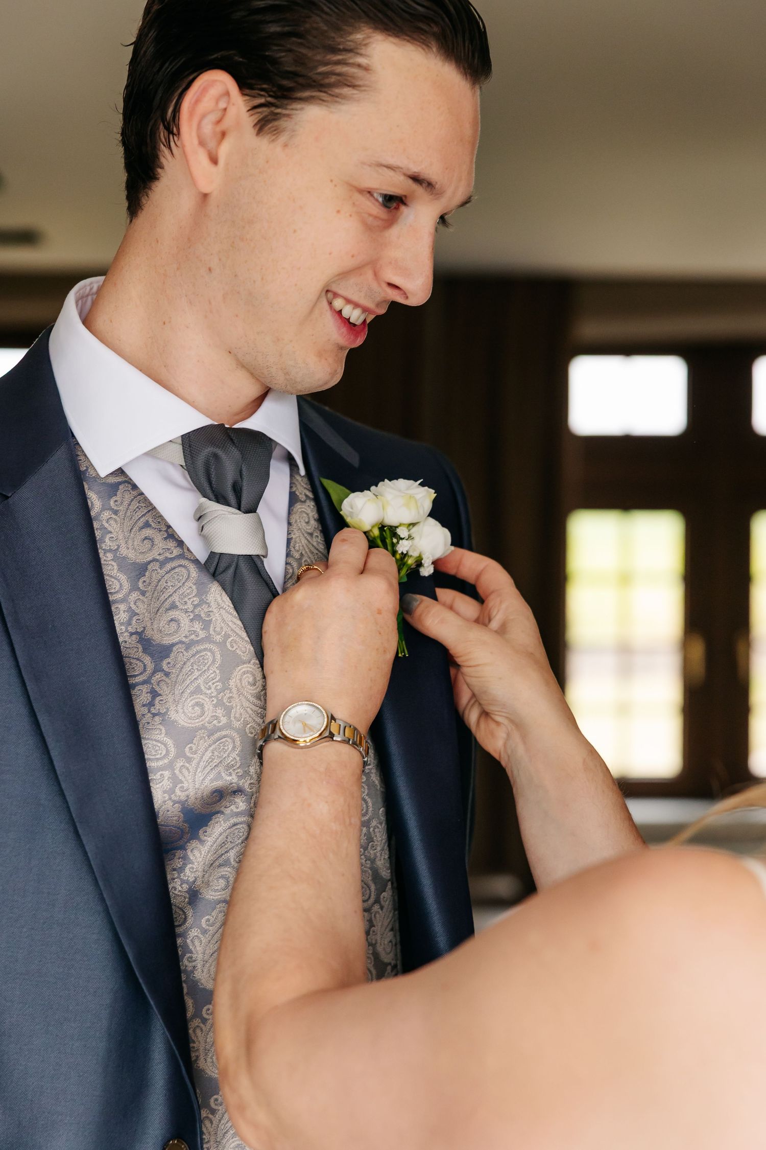 Smiling groom in navy suit having white floral boutonniere pinned to his lapel.